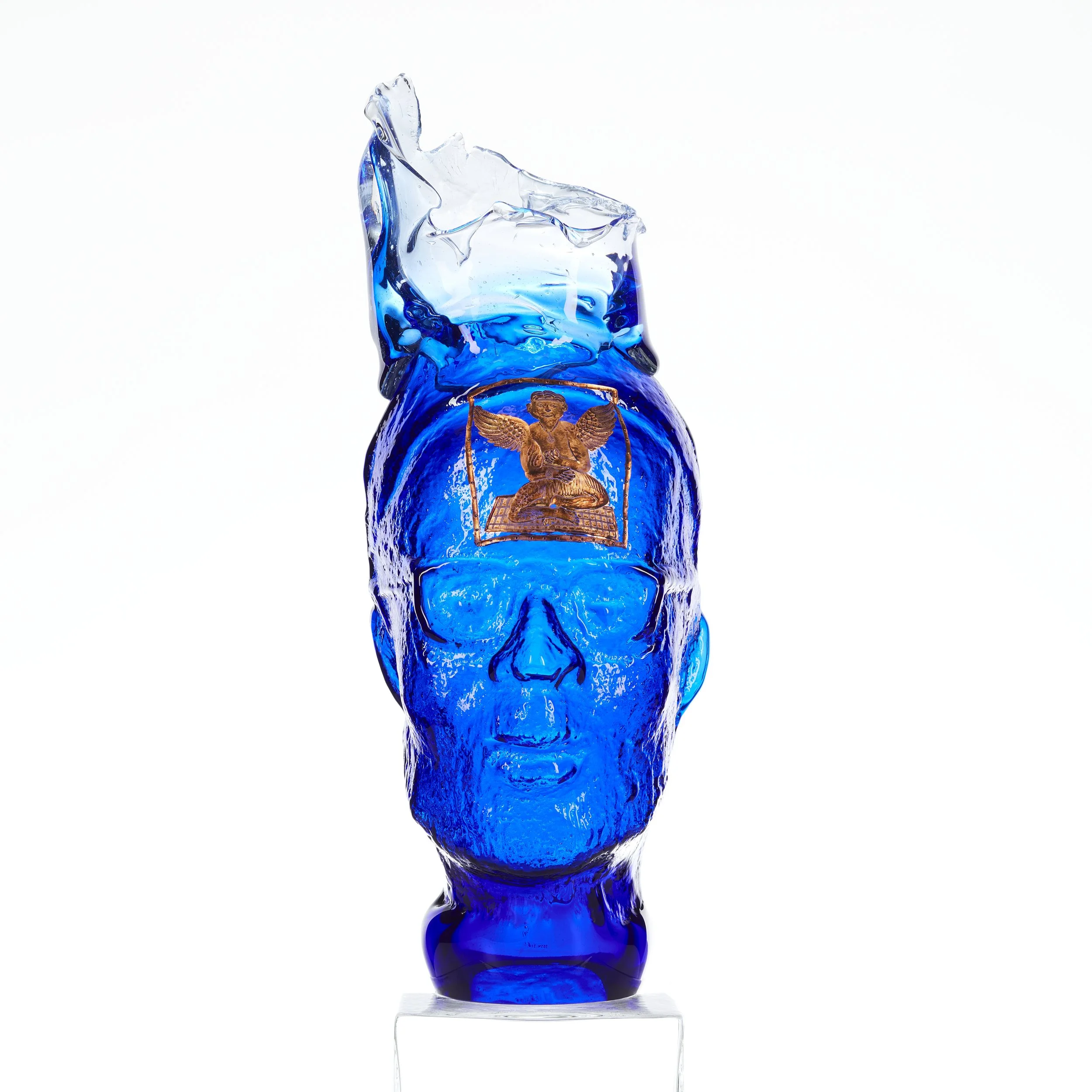 Glass blue bust of a man's head, on the forehead is a gold illustration. There is a partial cylindrical shape on top of the head.