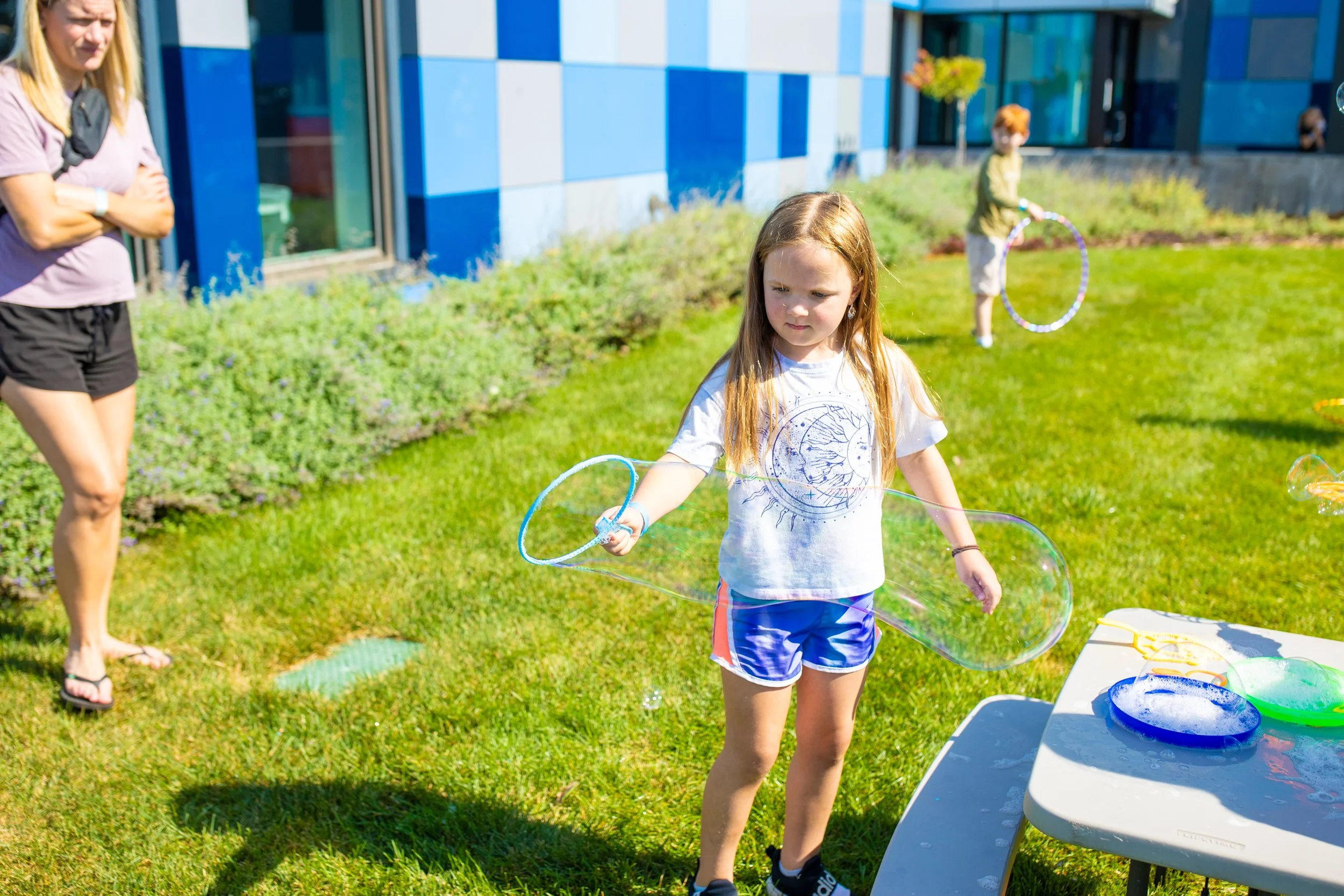 Children play with bubble wands on the CAT's front lawn area.