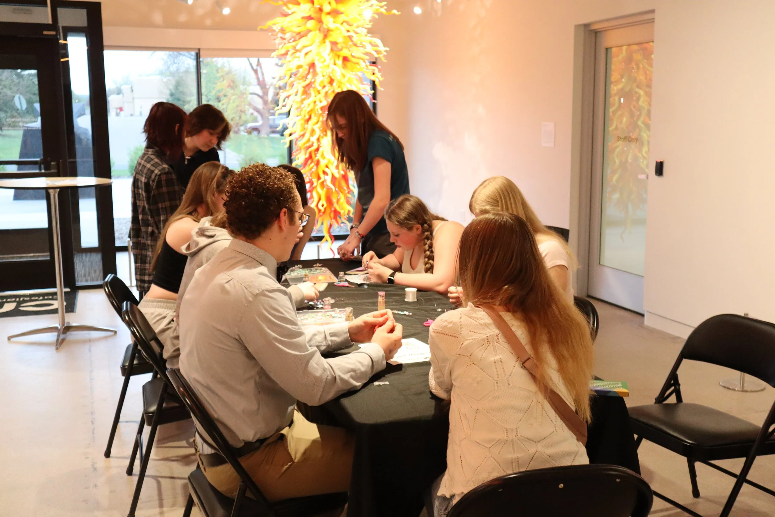 Teenagers gathered around a table intently working on a craft project.