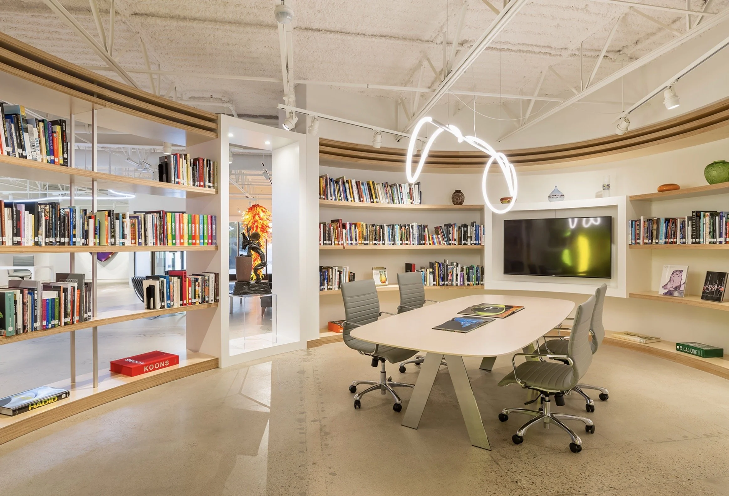 The museum library's large table surrounded by curved bookshelves and a rope-like light fixture above.