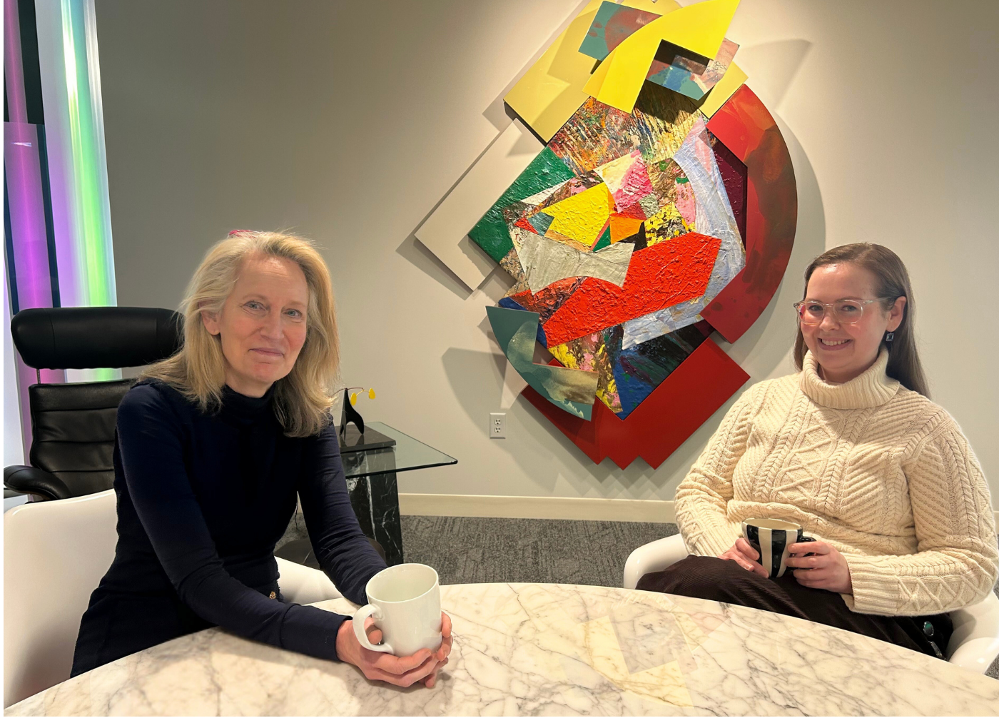 Curators Jill Ahlberg Yohe and Linnea Seidling seated a table holding coffee mugs.