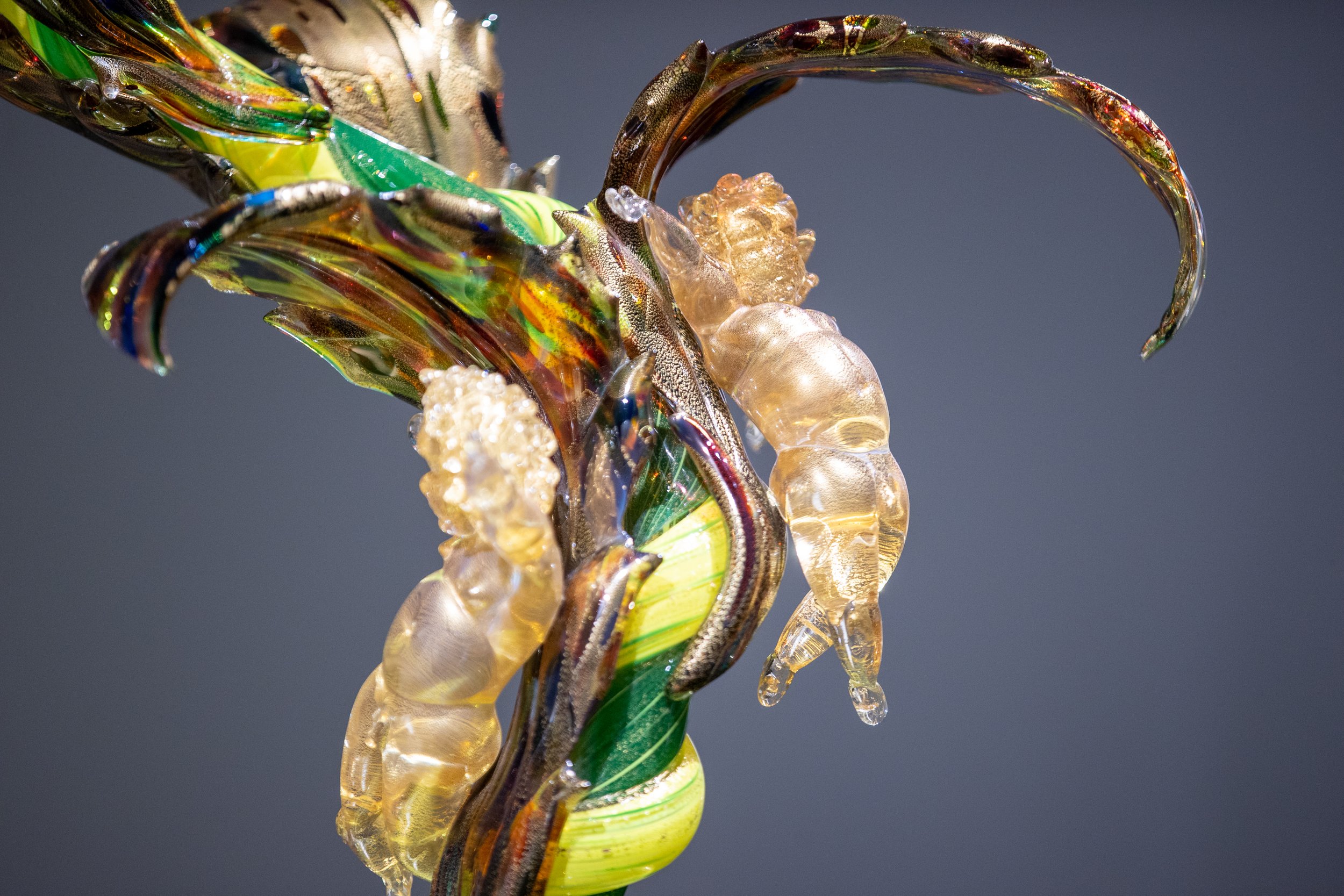 Close-up of a glass sculpture resembling a crab, featuring vibrant green, yellow, and brown colors with intricate details and a glossy finish.