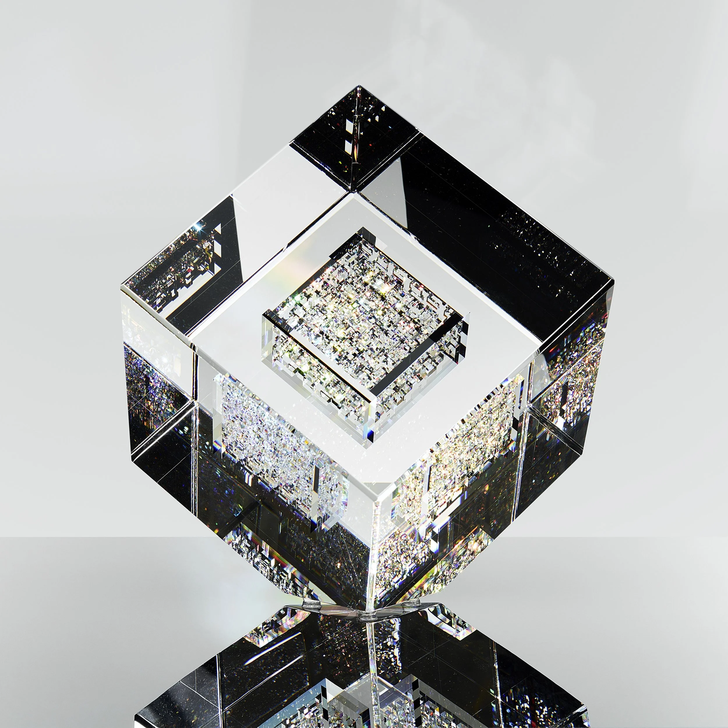 A square glass sculpture sitting on one of its corners and sparkling.
