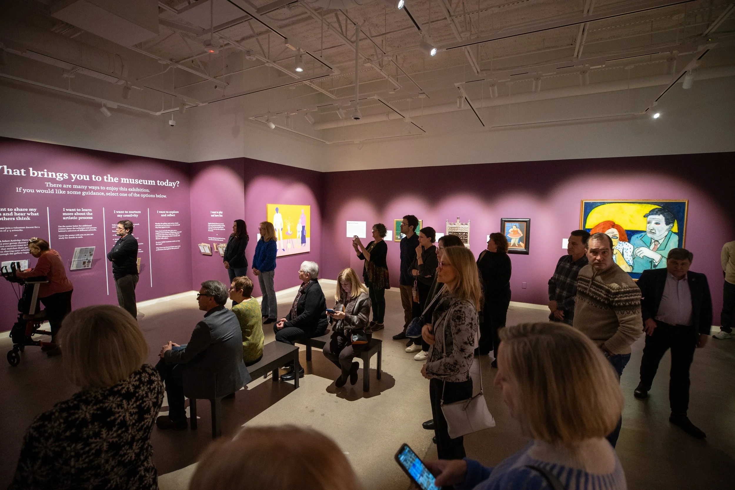 A large crowd gathers in the gallery, some sitting and some standing. 