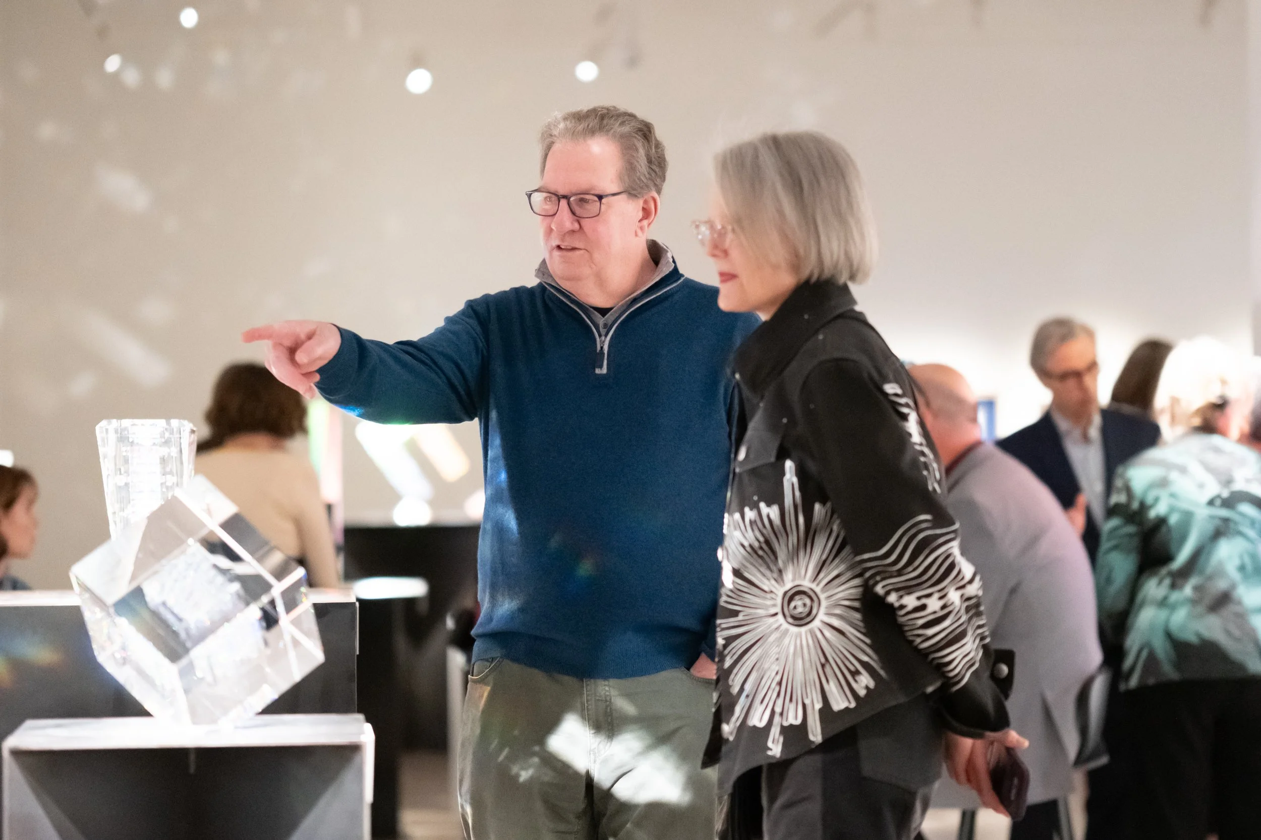 Two people look at a sculpture, the man points towards it. 