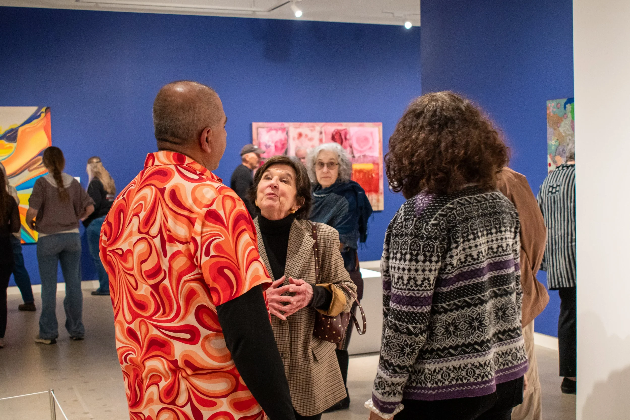 Group of people talking and observing artwork inside an art gallery with blue walls.