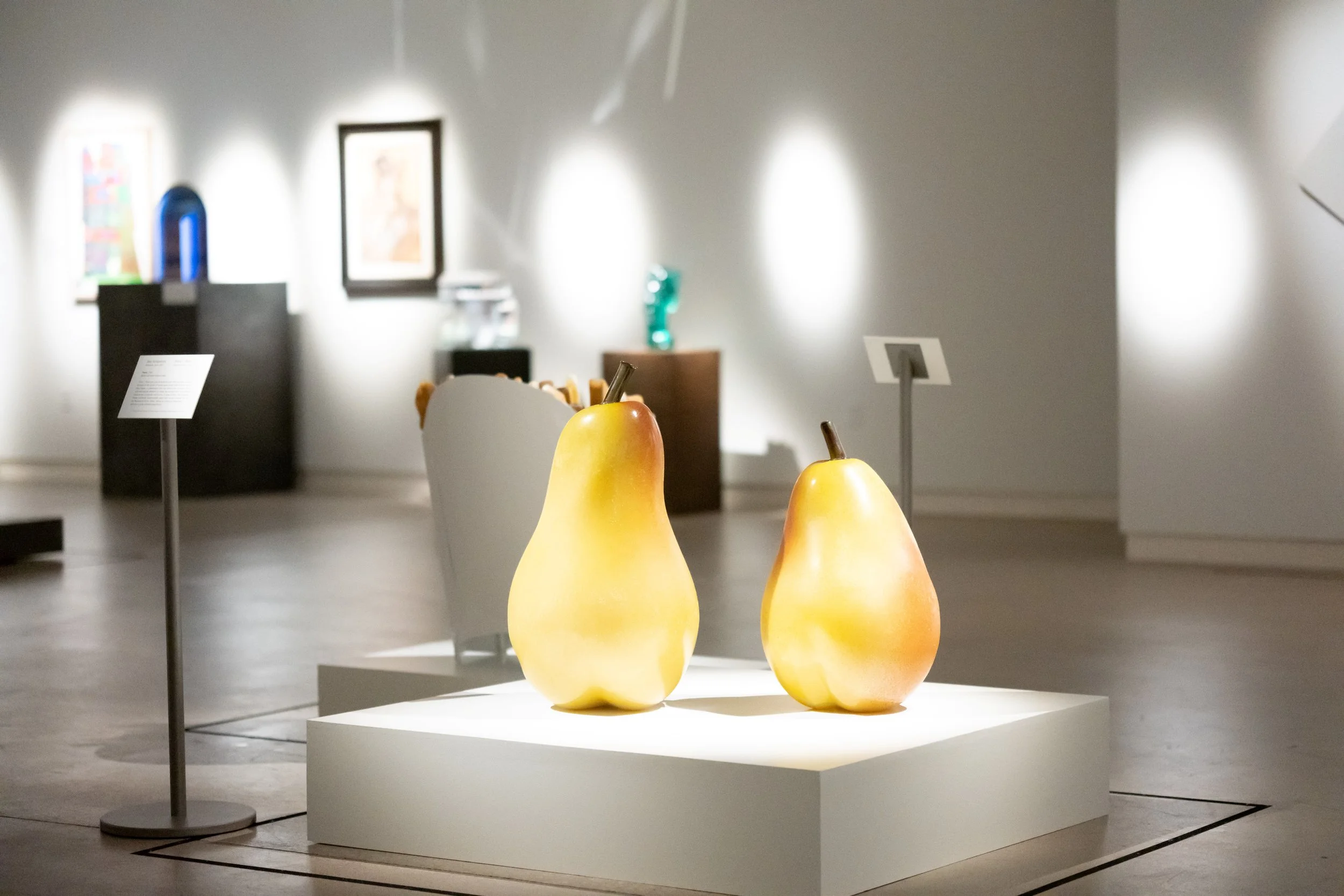 Two large pear sculptures on a platform in an exhibition gallery.