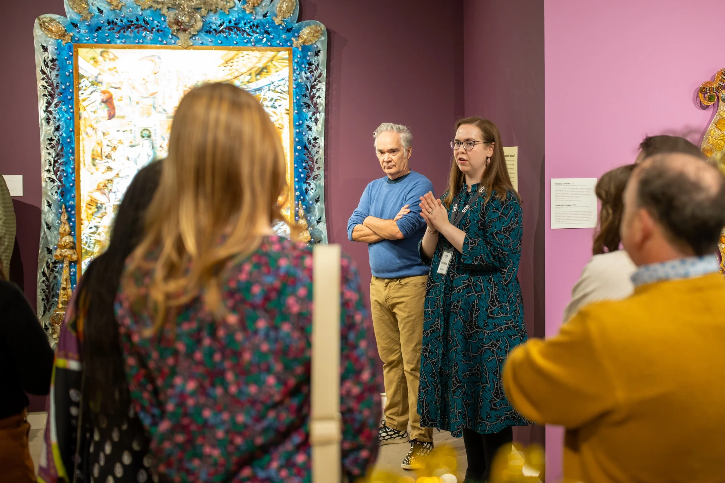 A museum curator speaking while standing next to artist Jamex de la Torre in the gallery.