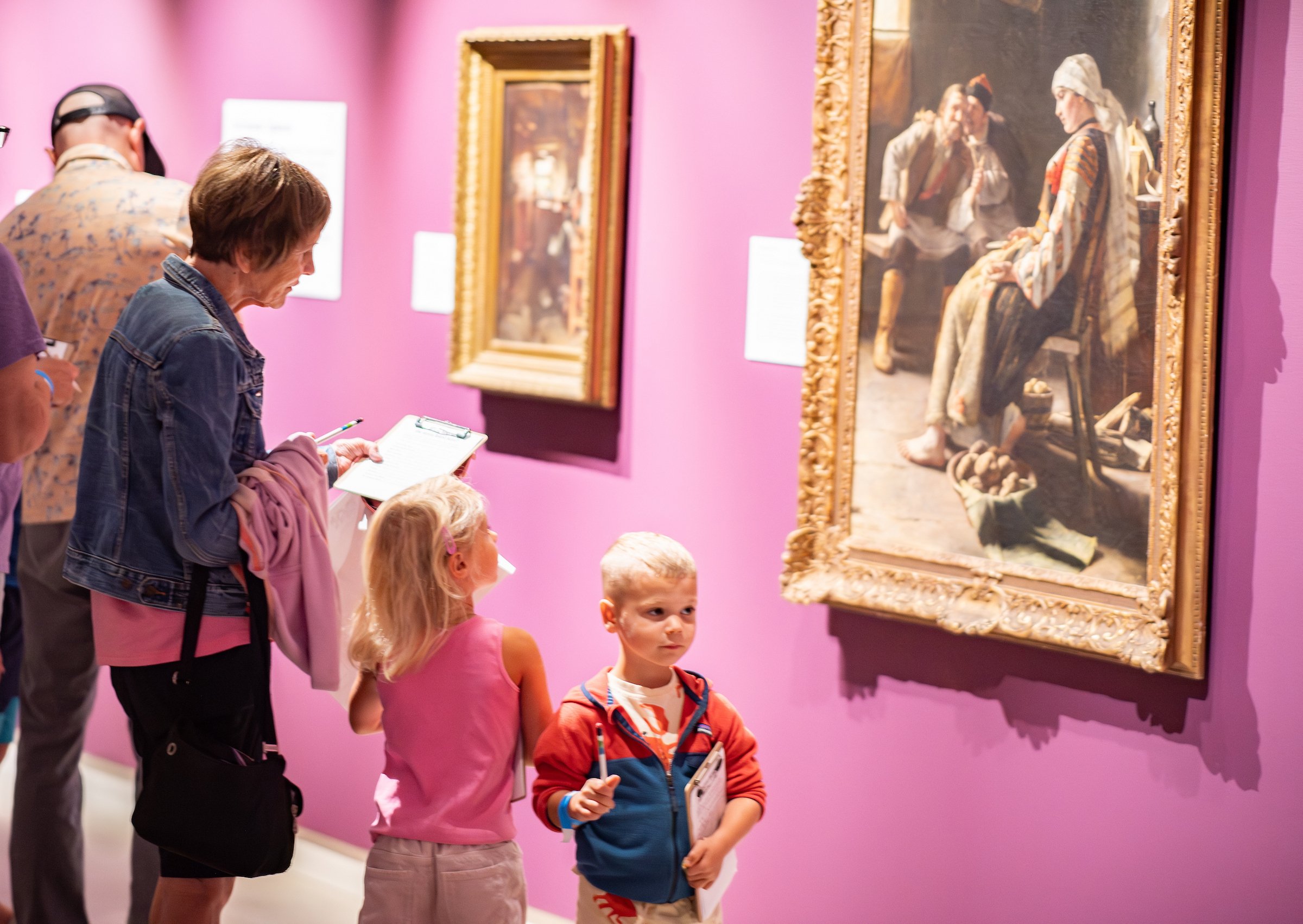 A grandmother works on a scavenger hunt in the gallery with two young children.