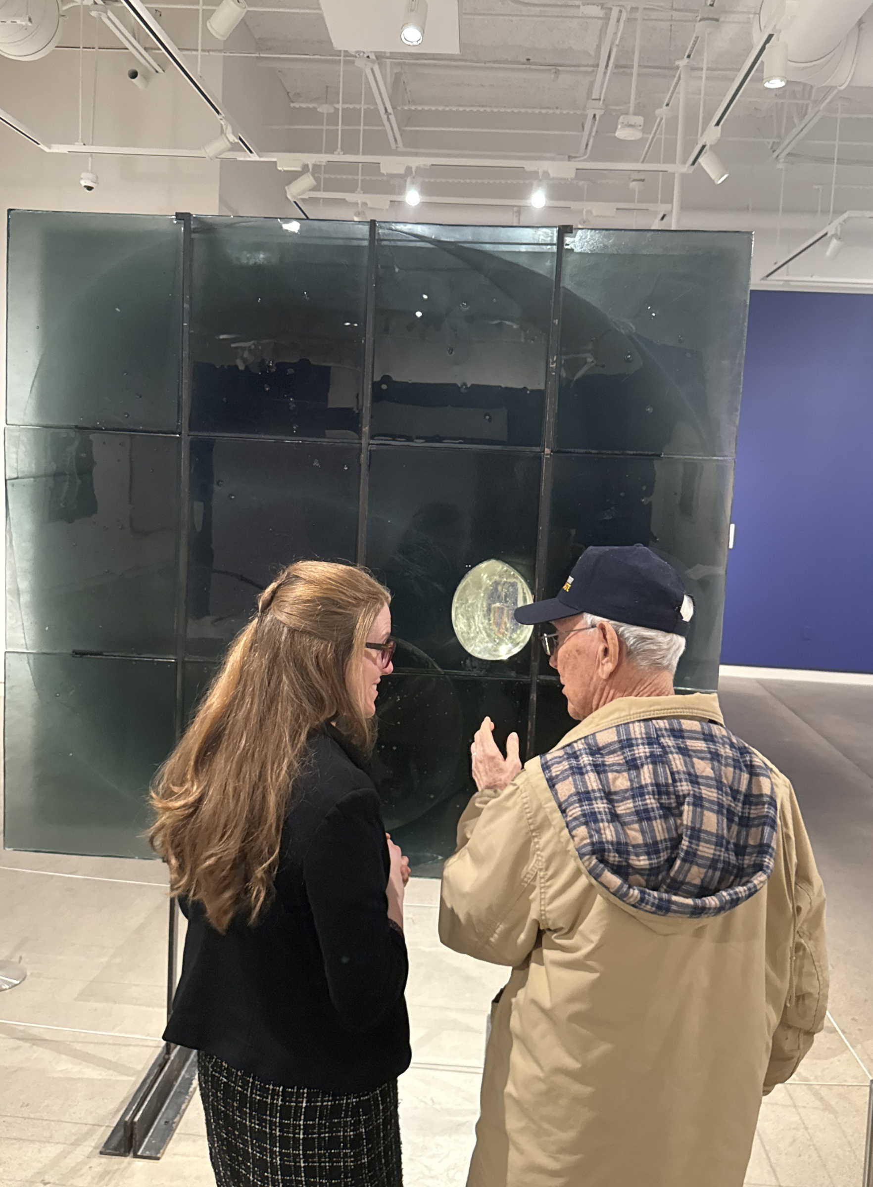 An older person holds hands with a younger person as they look at a glass sculpture together.