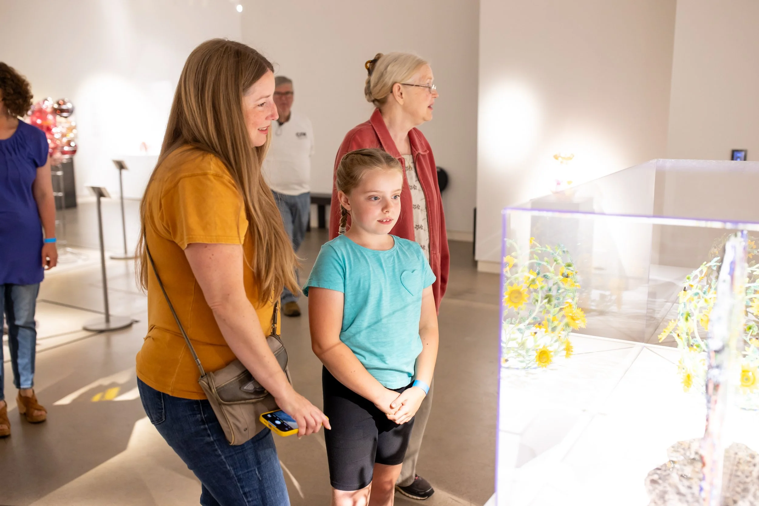 A family in the gallery studying a glass sculpture in a case.