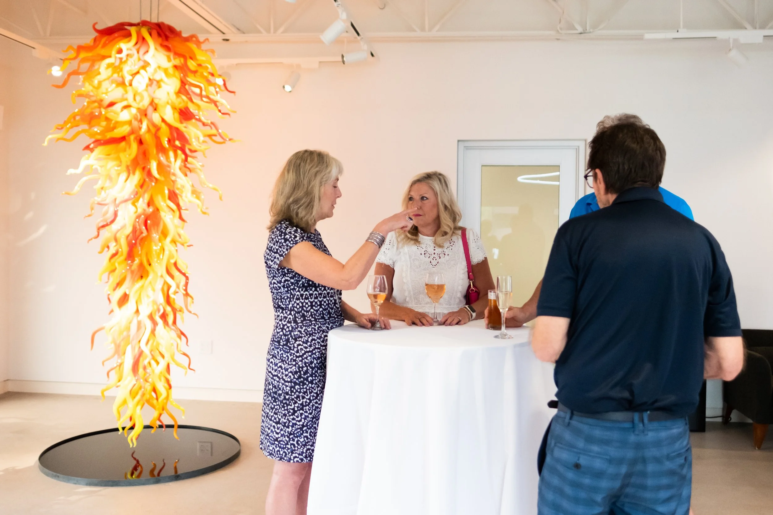 A small group gathers at a table with drinks, Cafesjian Chandelier by Dale Chihuly can be seen in the background. 
