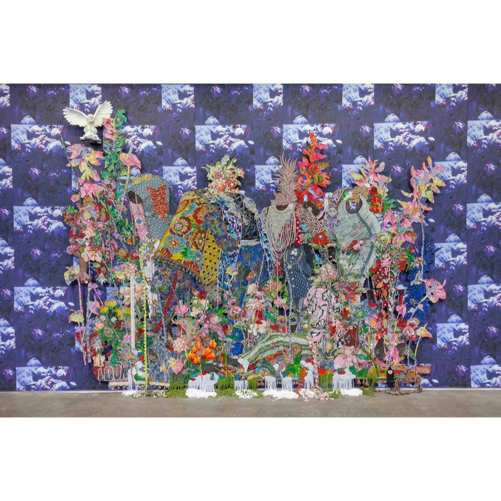 A mixed media art installation featuring embroidered and fabric artwork of elephants, set against a deep blue floral backdrop in a gallery space.