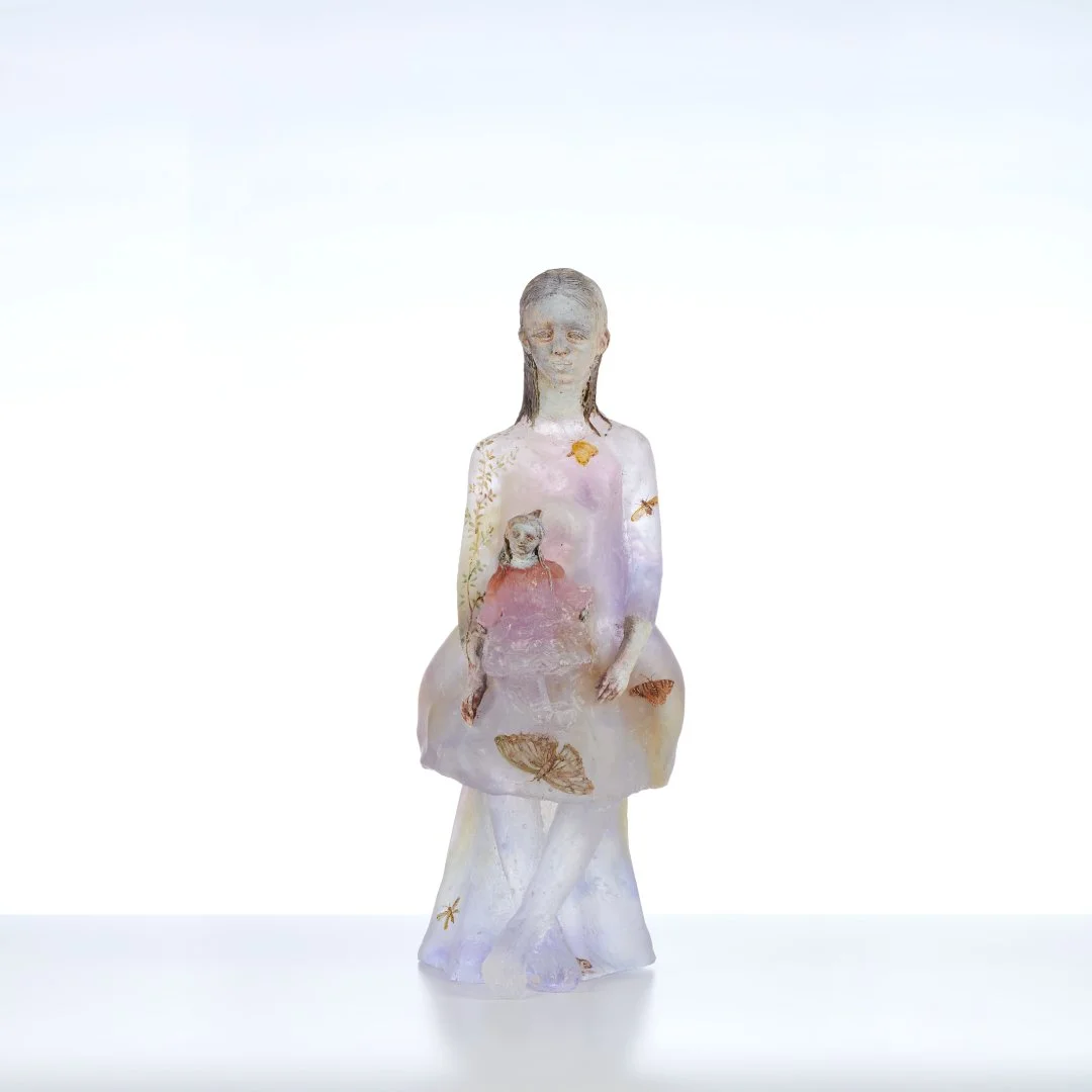 A statue of a woman with closed eyes holding a small child, decorated with butterflies and floral patterns. The statue has a soft, translucent appearance.