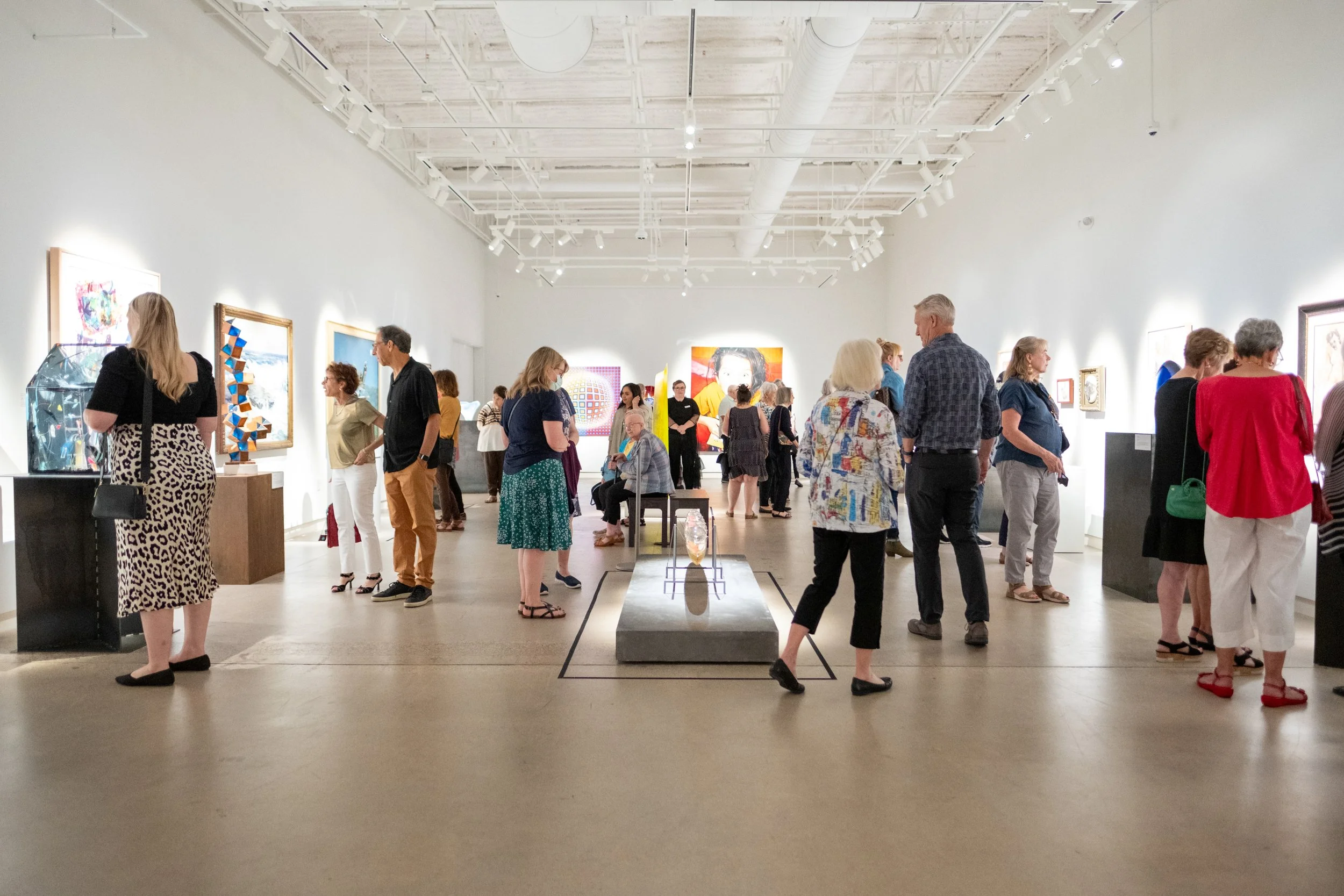 People gathered in a gallery, looking at various artworks. 