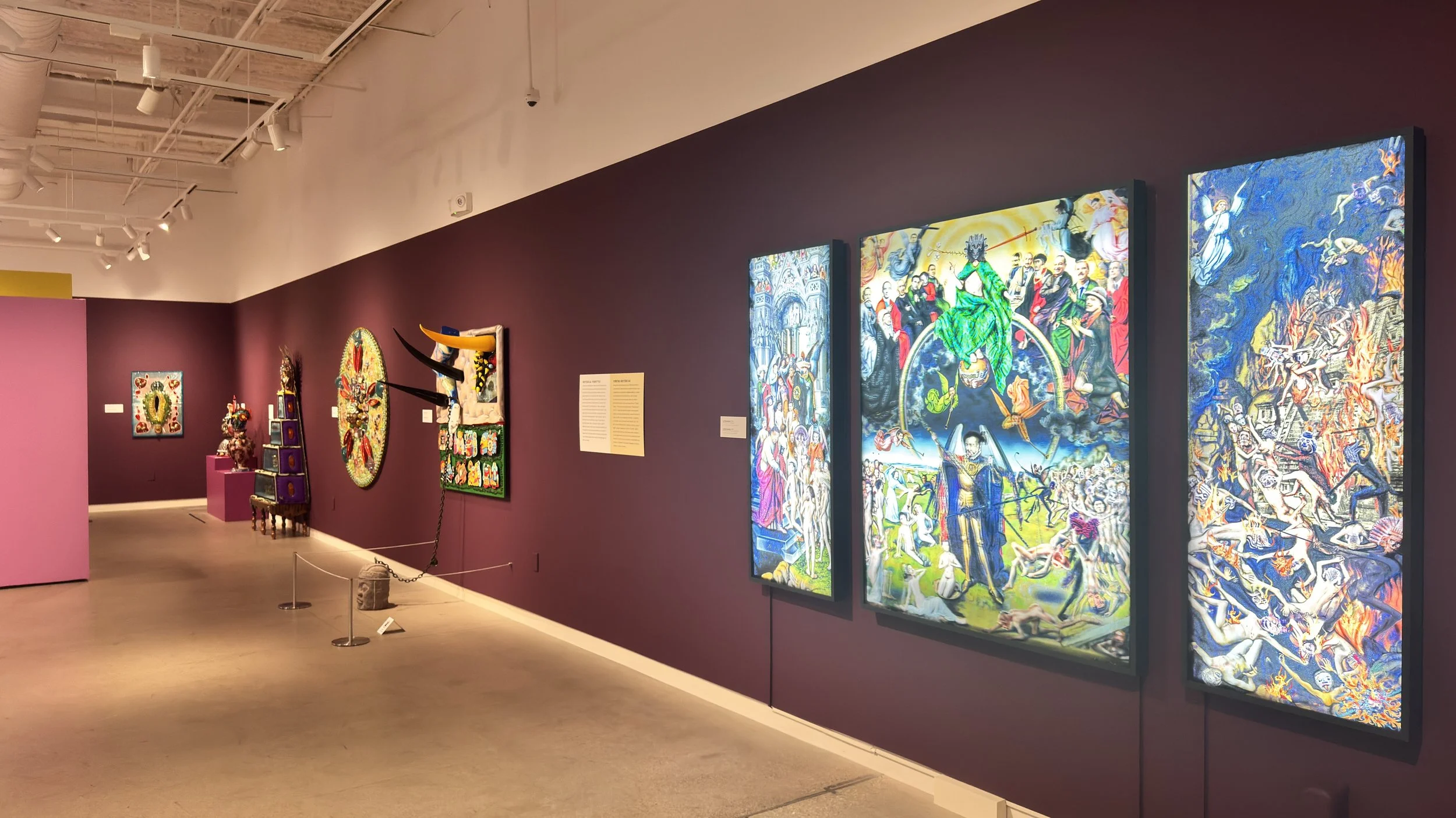 Art gallery exhibit featuring colorful paintings on purple walls, including religious and mythological themes, with sculptures and decorative objects on display.