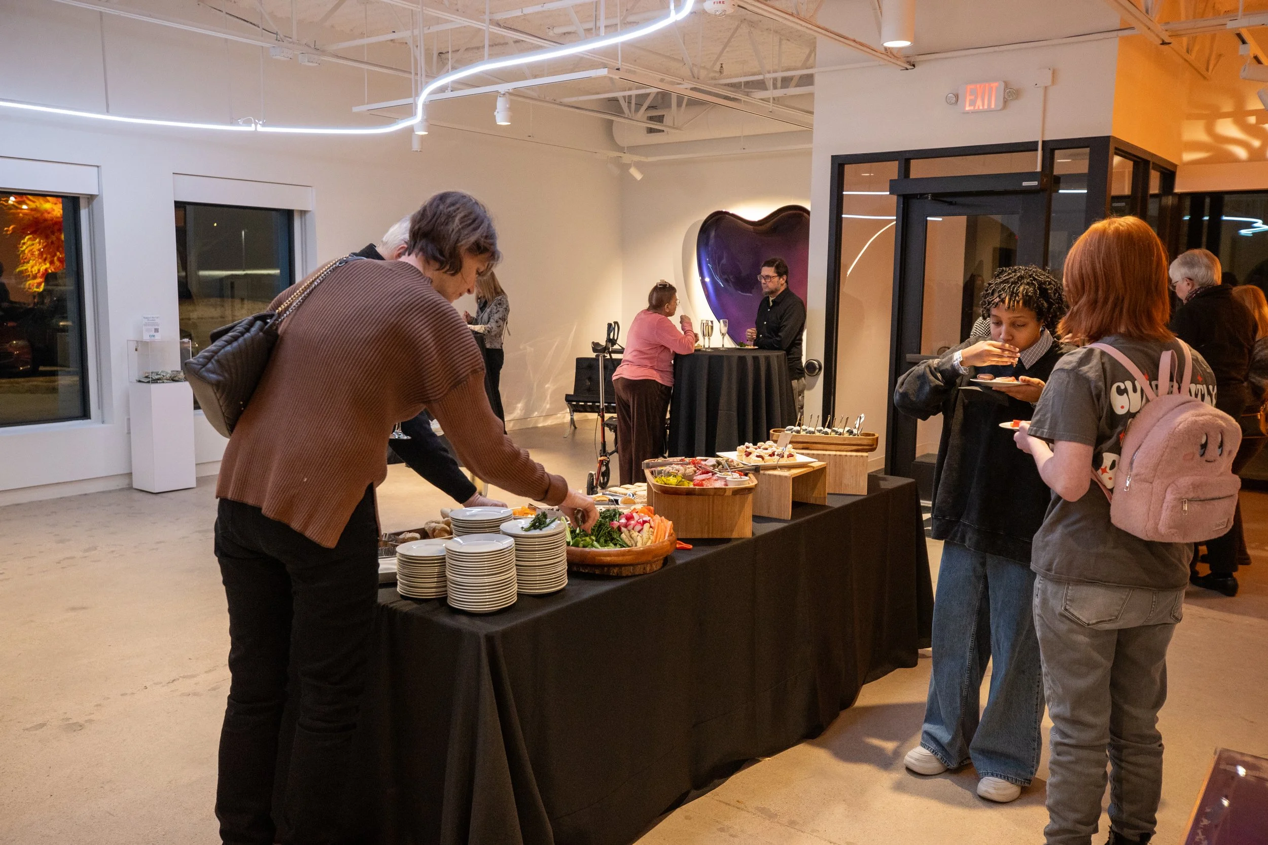 People stand around a table with a large array of food. 