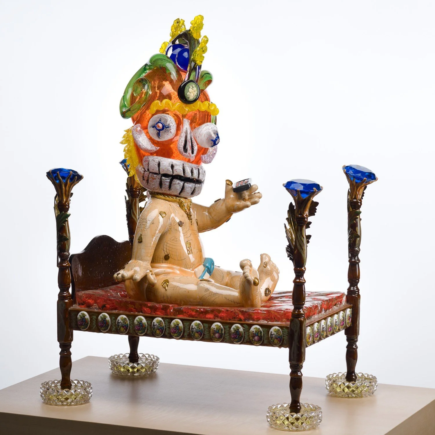 Glass sculpture of a baby holding a remote and wearing an orange luchador mask sitting on a four post bed.