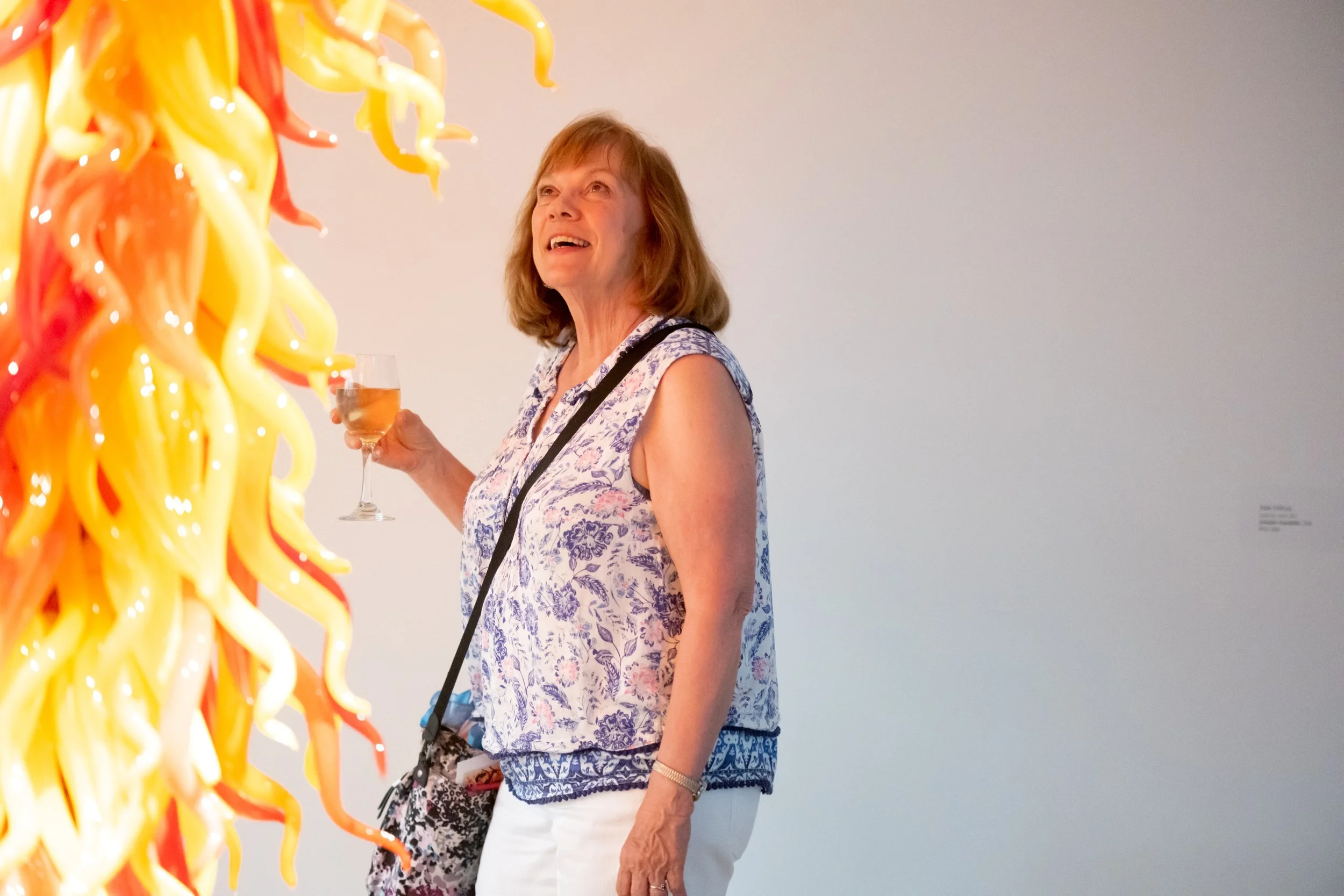 A woman holding a drink looks at Cafesjian Chandelier by Dale Chihuly. 