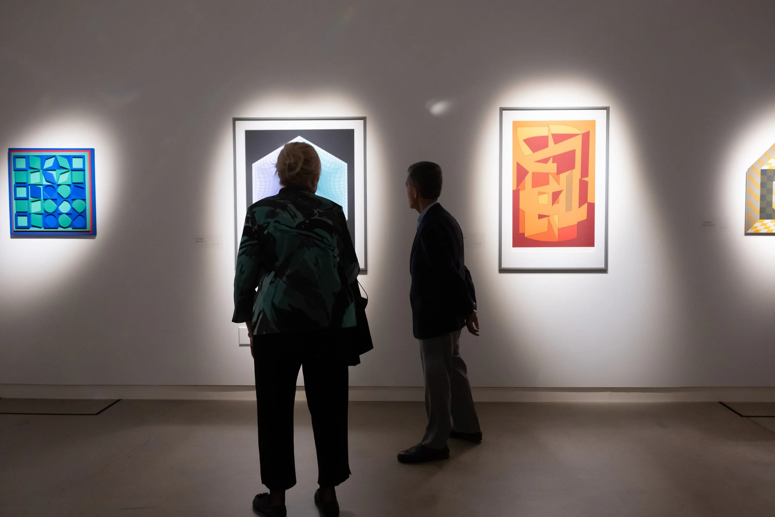 Two people in the gallery look at artwork on the wall. 