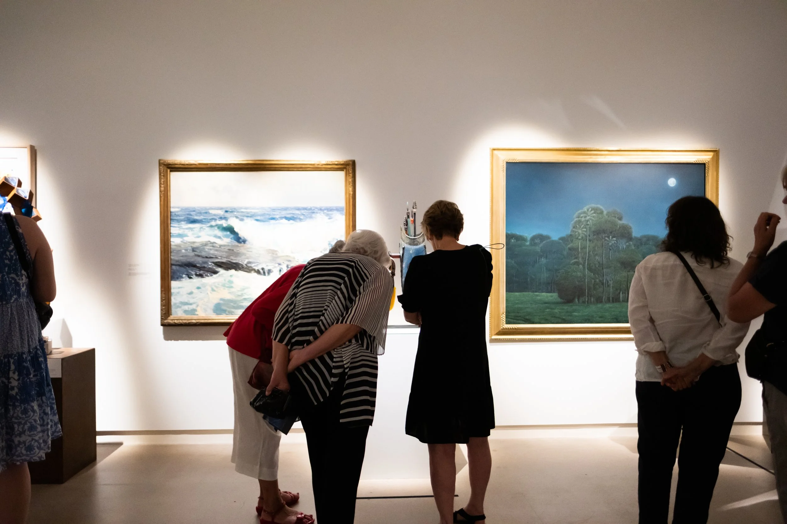 People in the gallery look at sculptures and paintings. 