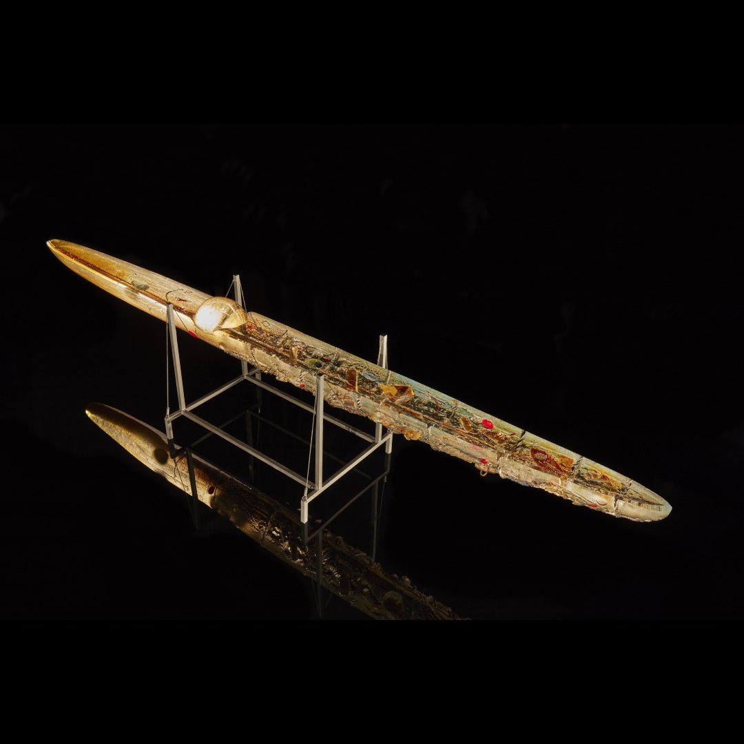 An oblong glass boat sculpture with human-like figures inside.
