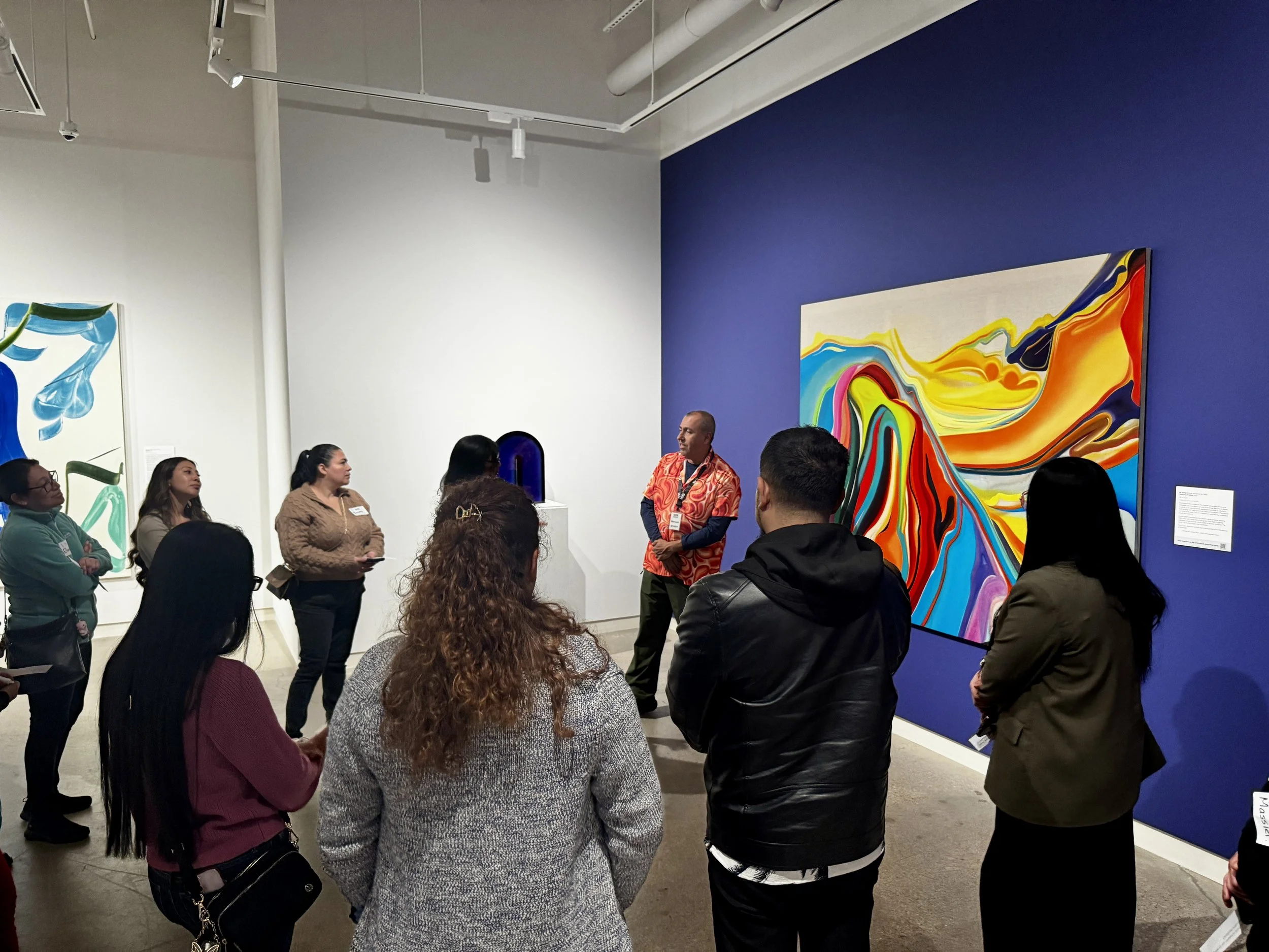 A group of adults gather around and discuss artwork in the gallery.