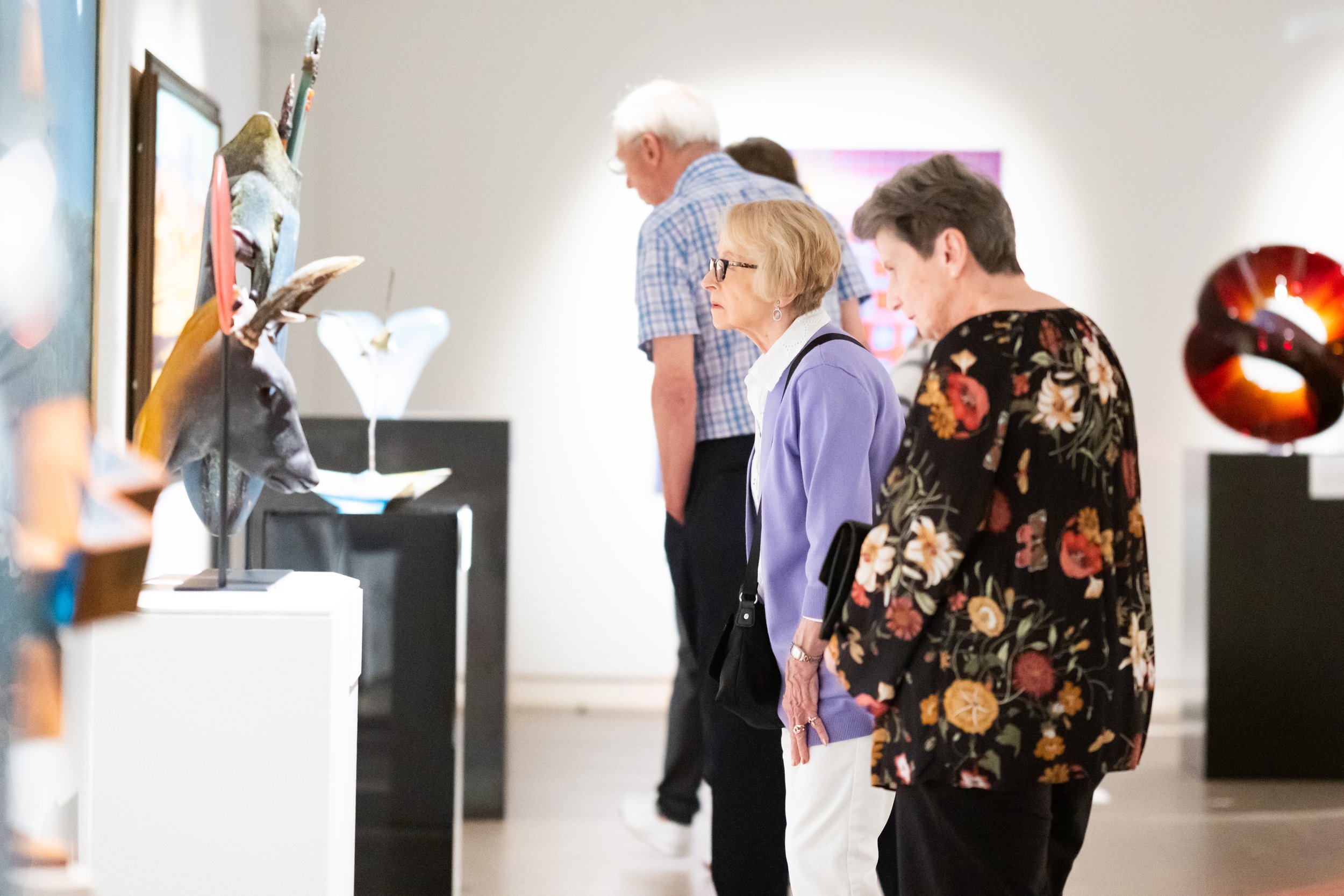 People in the gallery look at sculptures. 