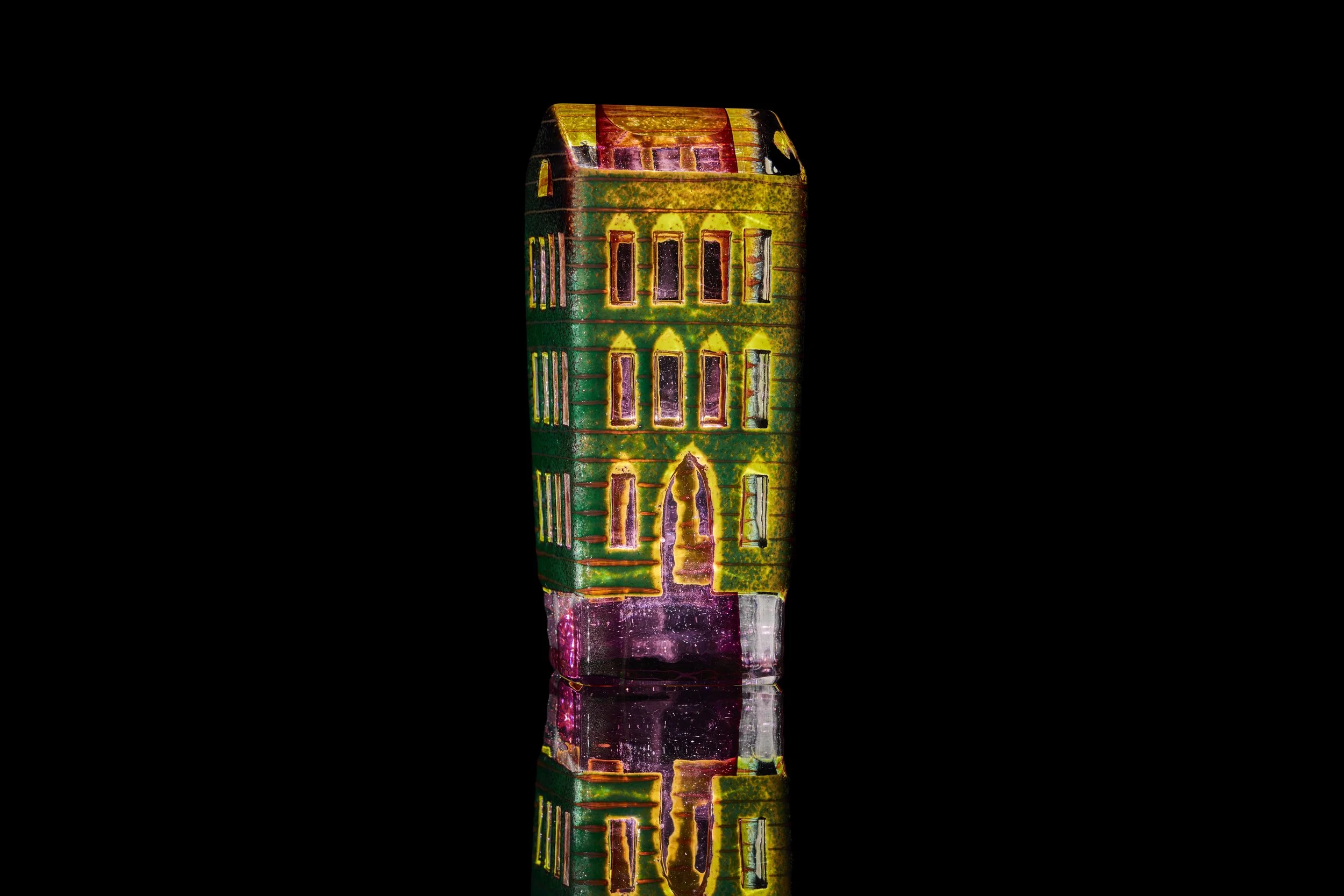 A glass sculpture that looks like a tall green, yellow, and purple building.