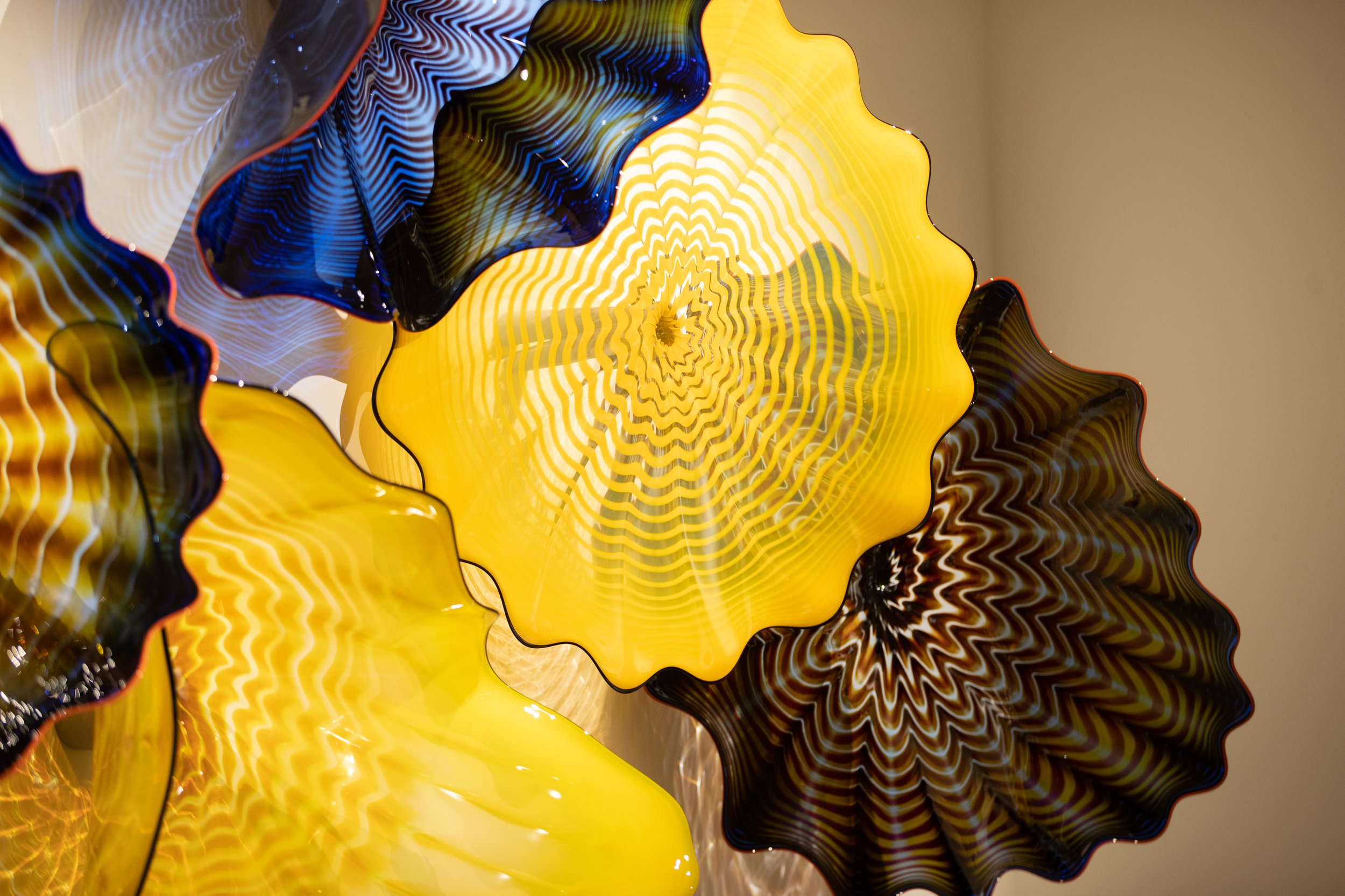 Colorful glass art with yellow, black, and blue wavy patterns and textured design, resembling flower-like shapes.
