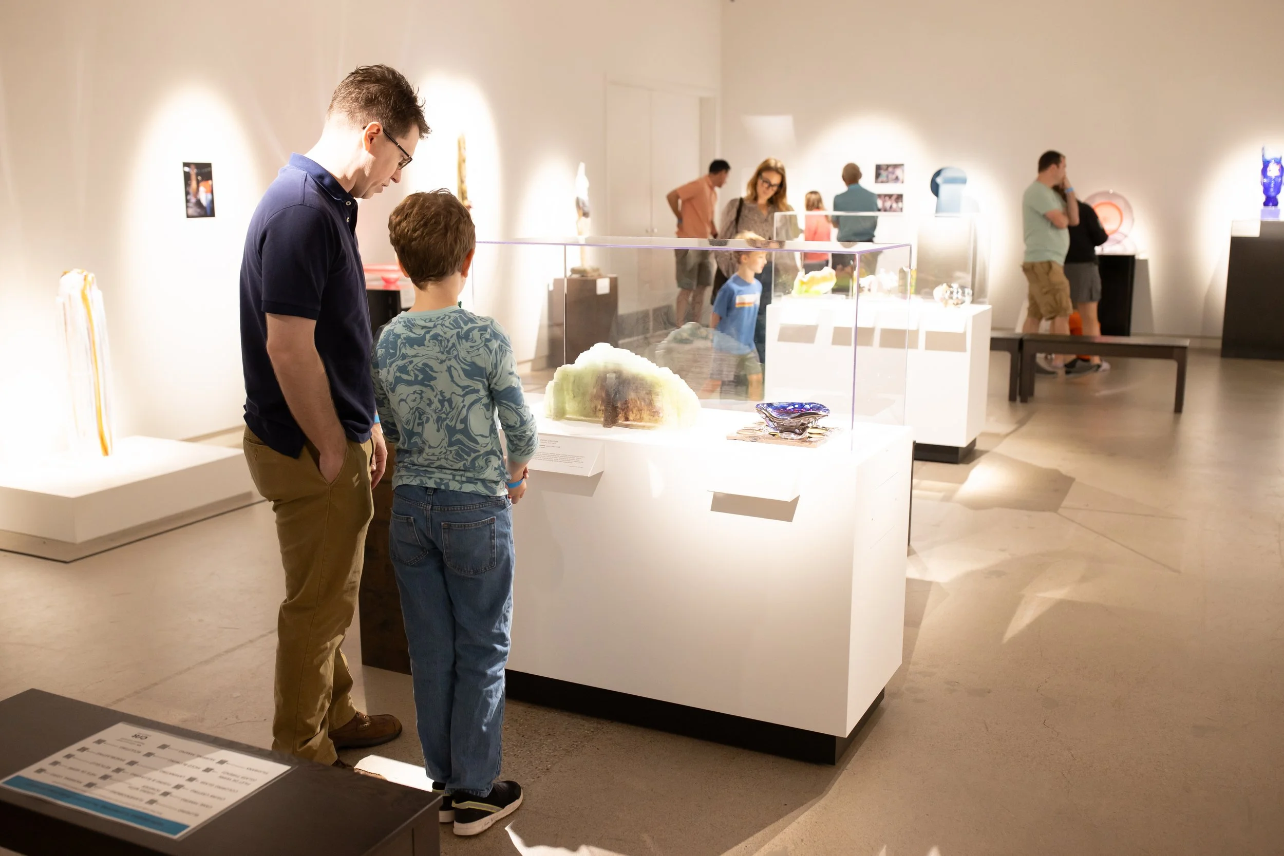 A parent and child studying a glass sculpture inside the museum gallery.