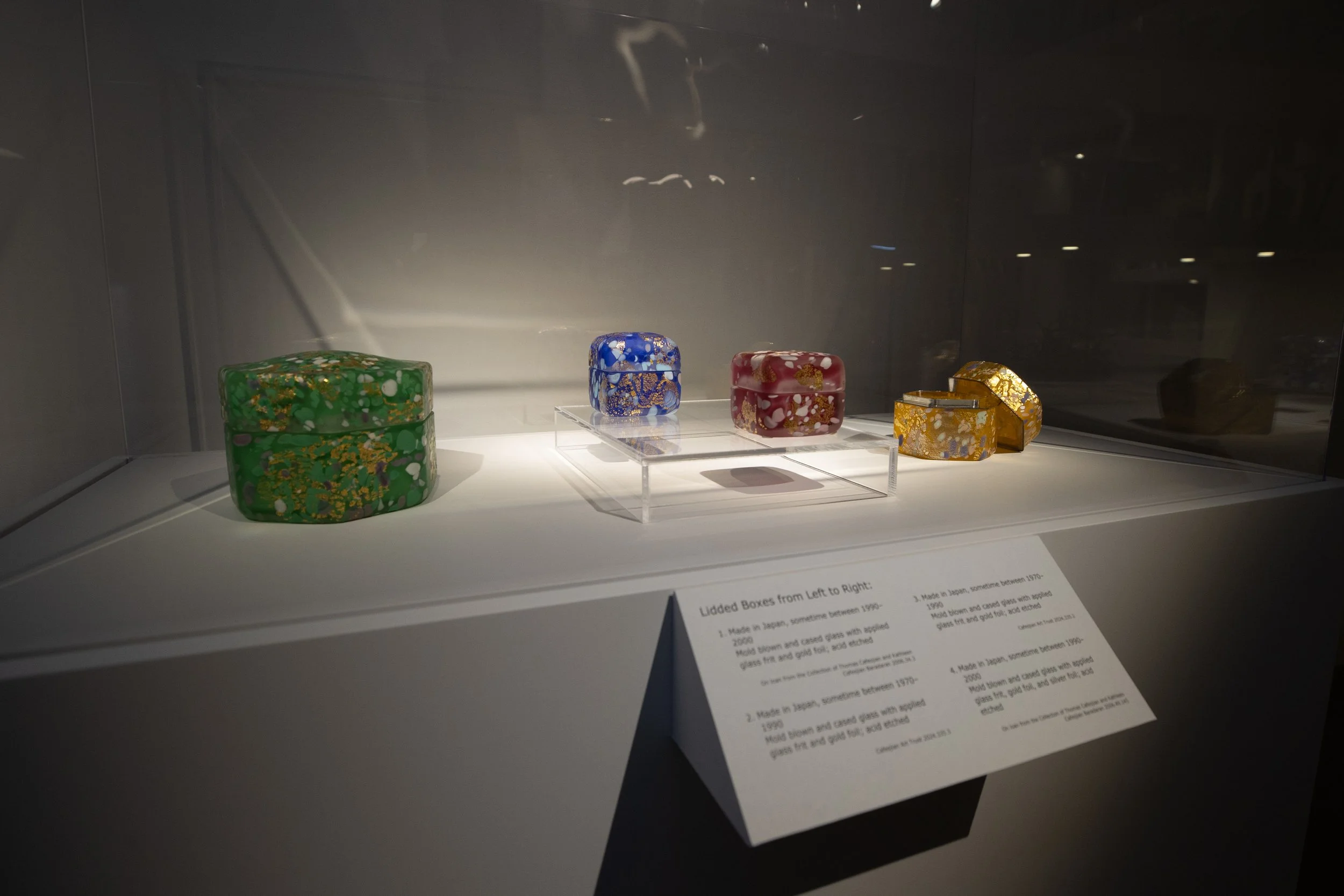 Display of colorful, ornate glass boxes arranged on a shelf in a museum exhibit.
