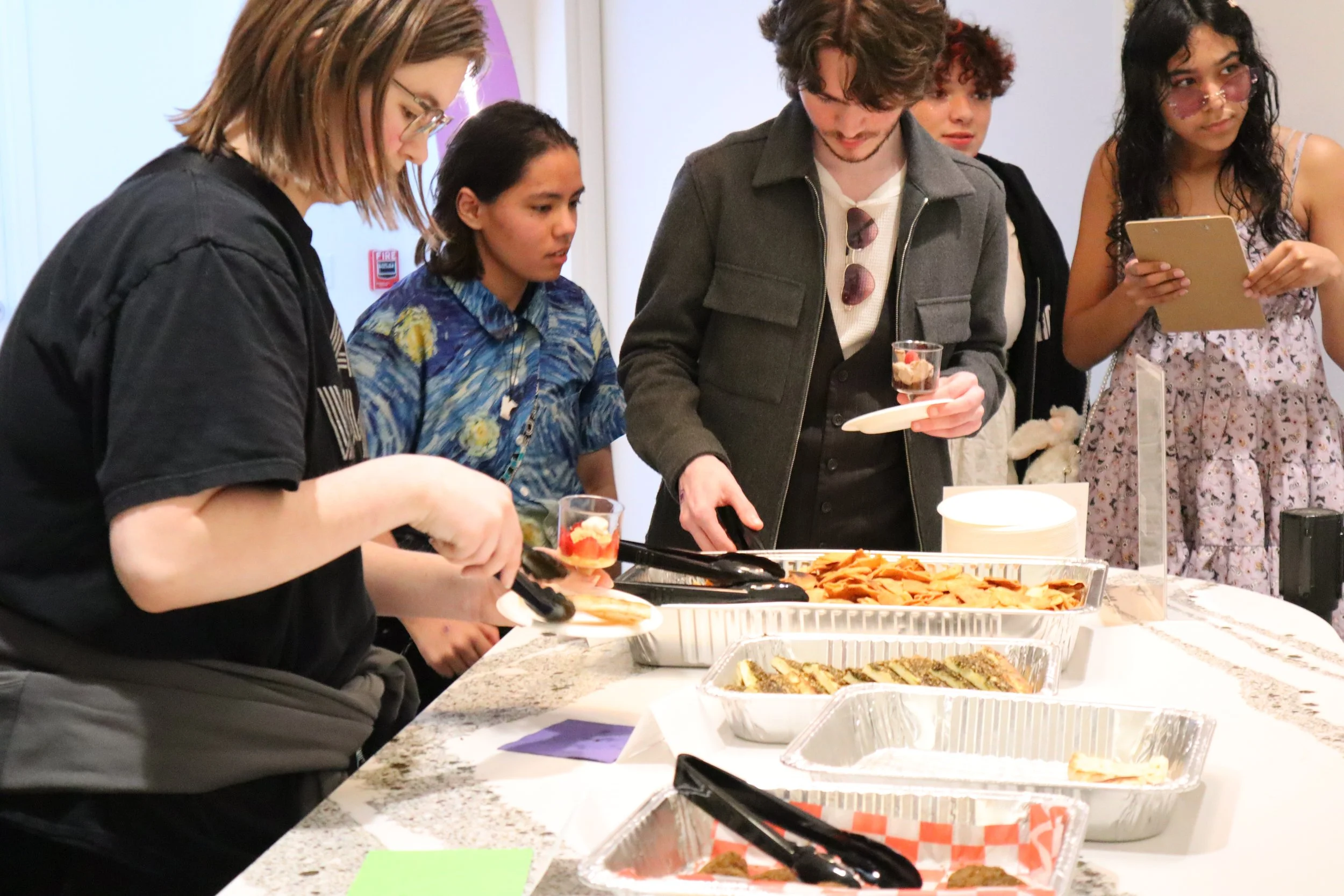 Teenagers helping themselves to food in large catering trays.