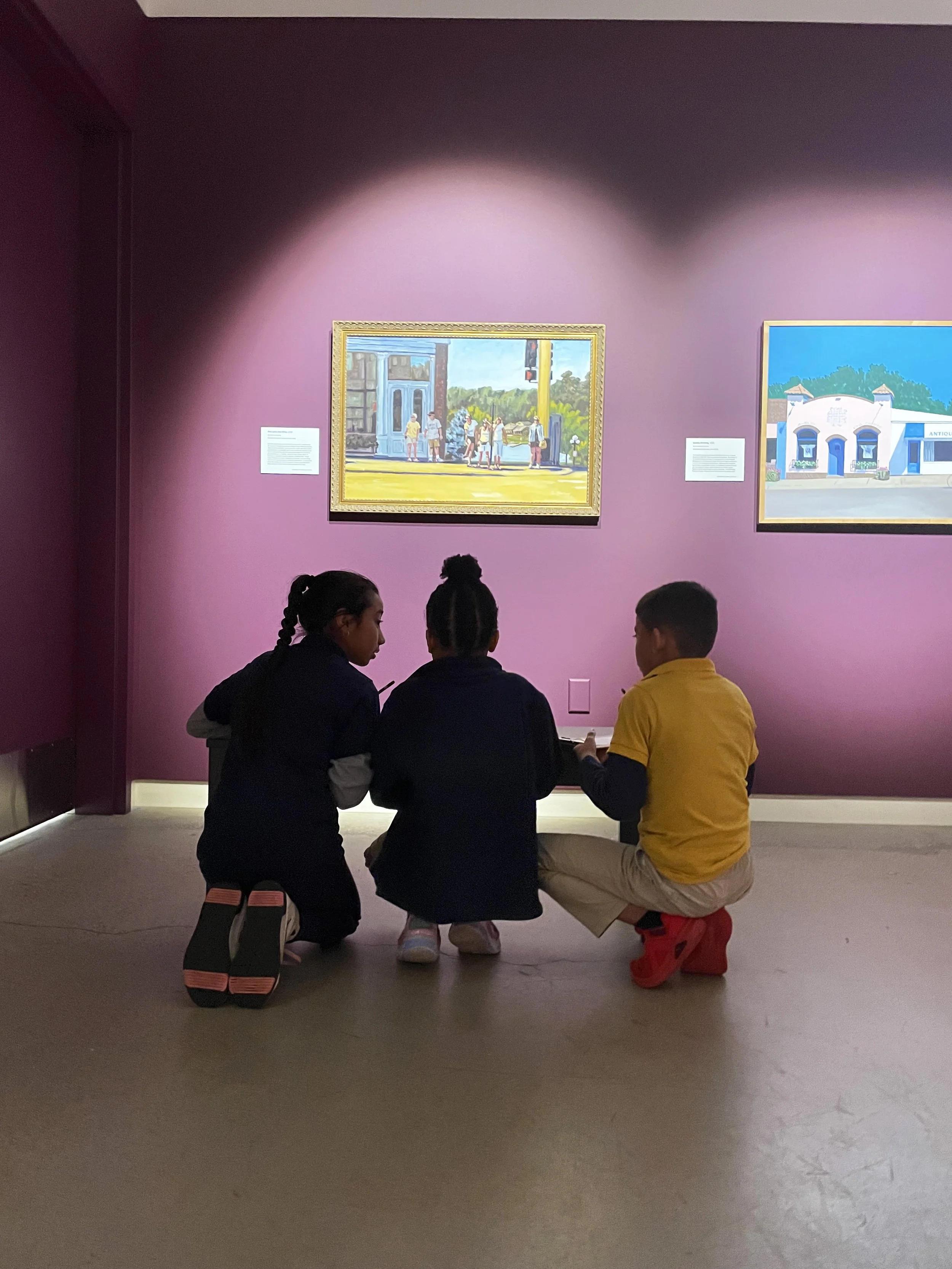 Three children crouched around a bench in the museum gallery working on a writing assignment.