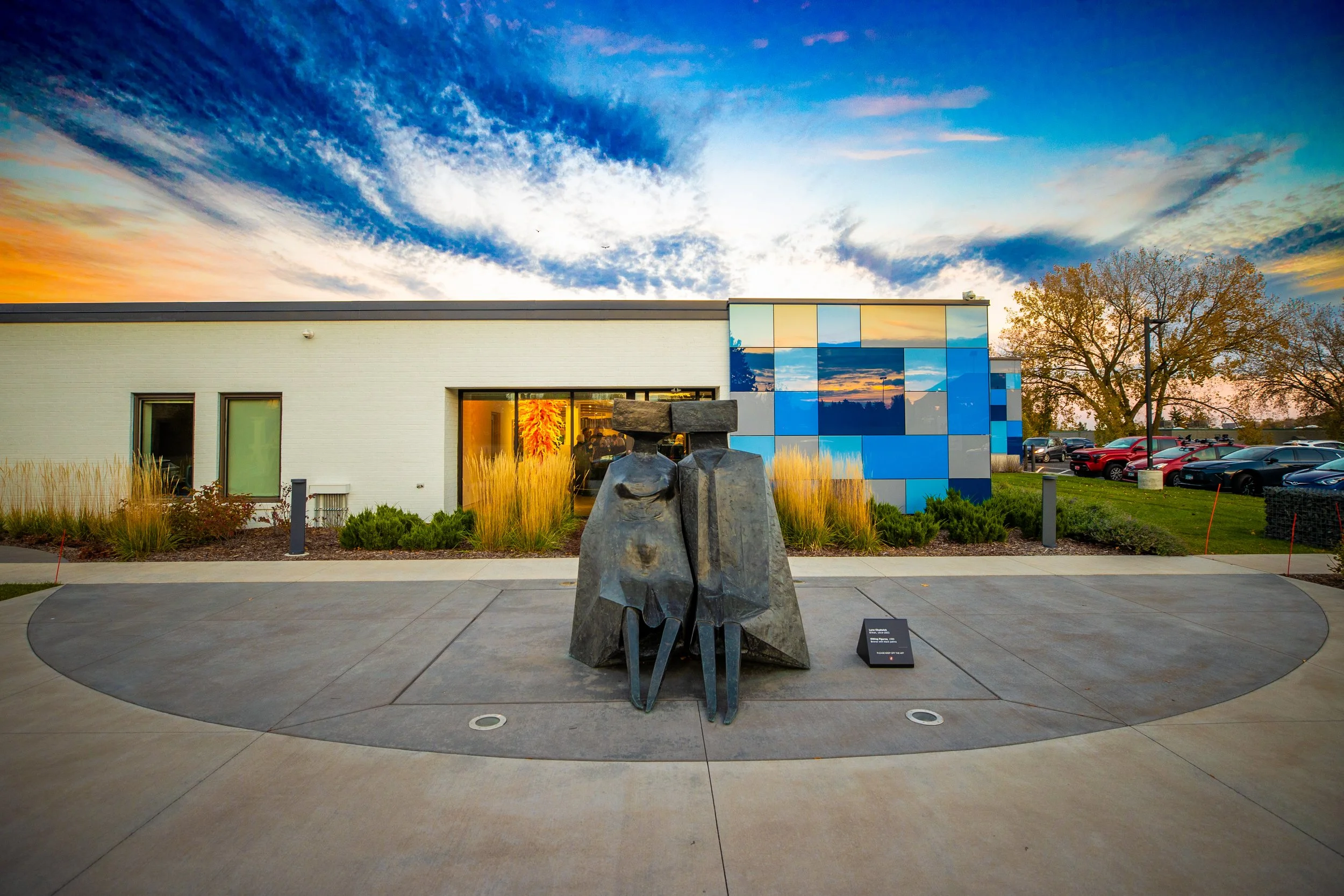A large bronze sculpture of two seated figures, placed on the patio outside the museum at sunset.