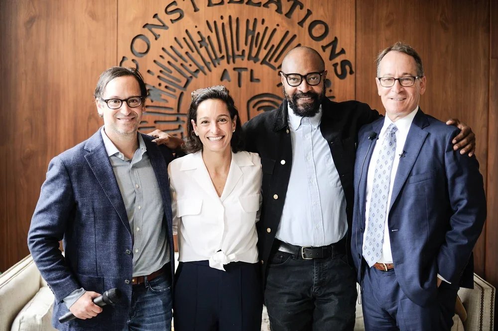 Four diverse professionals standing together in a room with wooden walls and a logo behind them reading 'Foundations.' They are smiling and appear to be at a formal or semi-formal event.