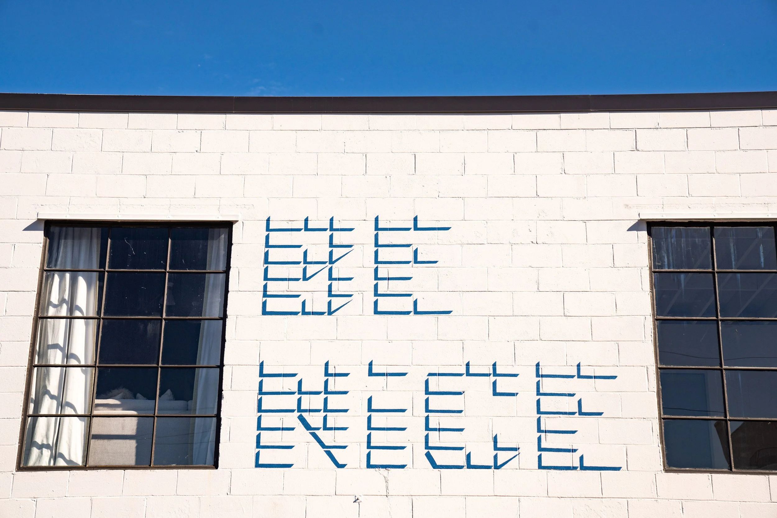 White building with two windows and blue geometric wall art, under a clear blue sky.