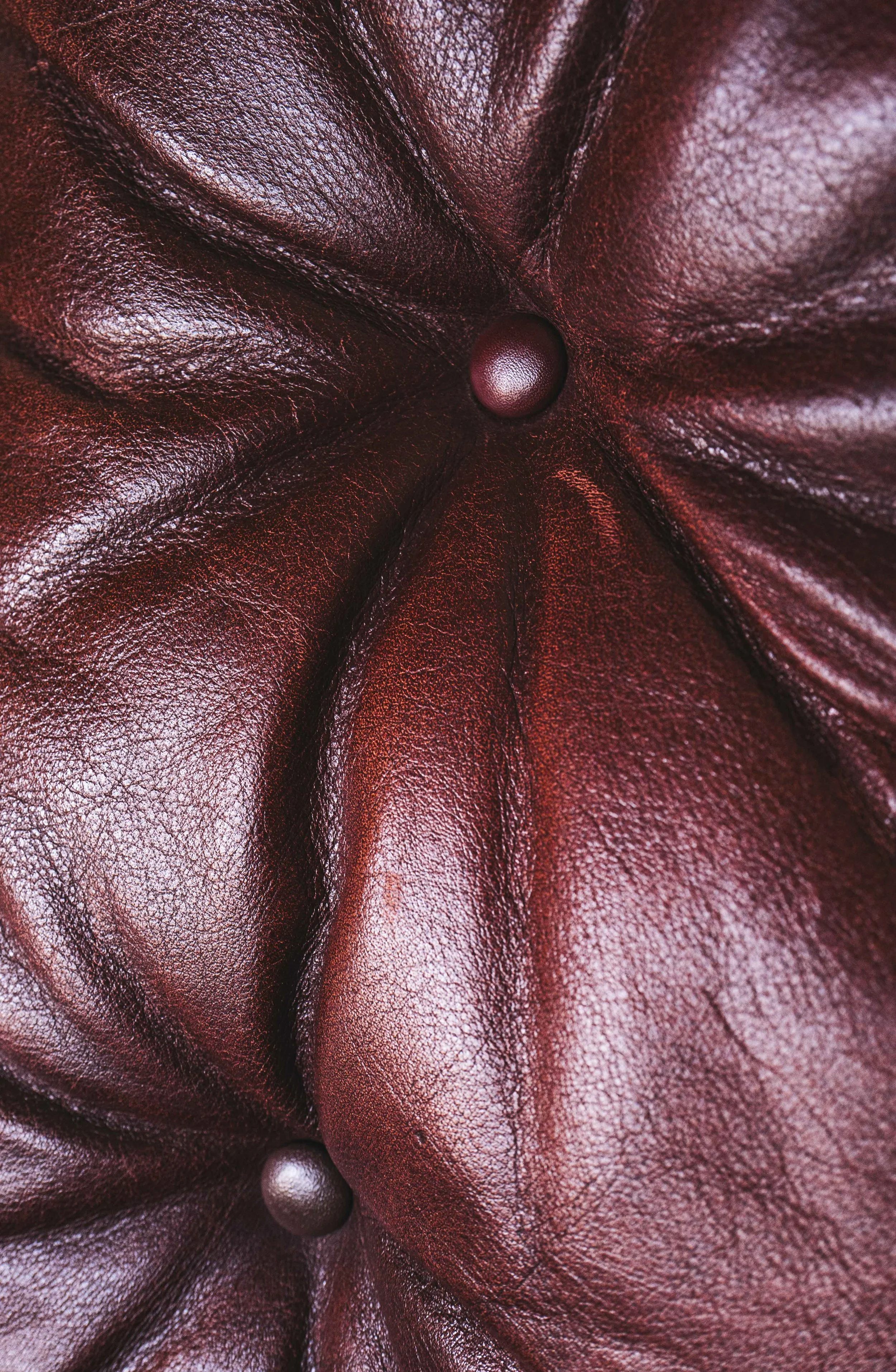 Close-up of a textured, burgundy leather fabric with a central button, gathered in folds.