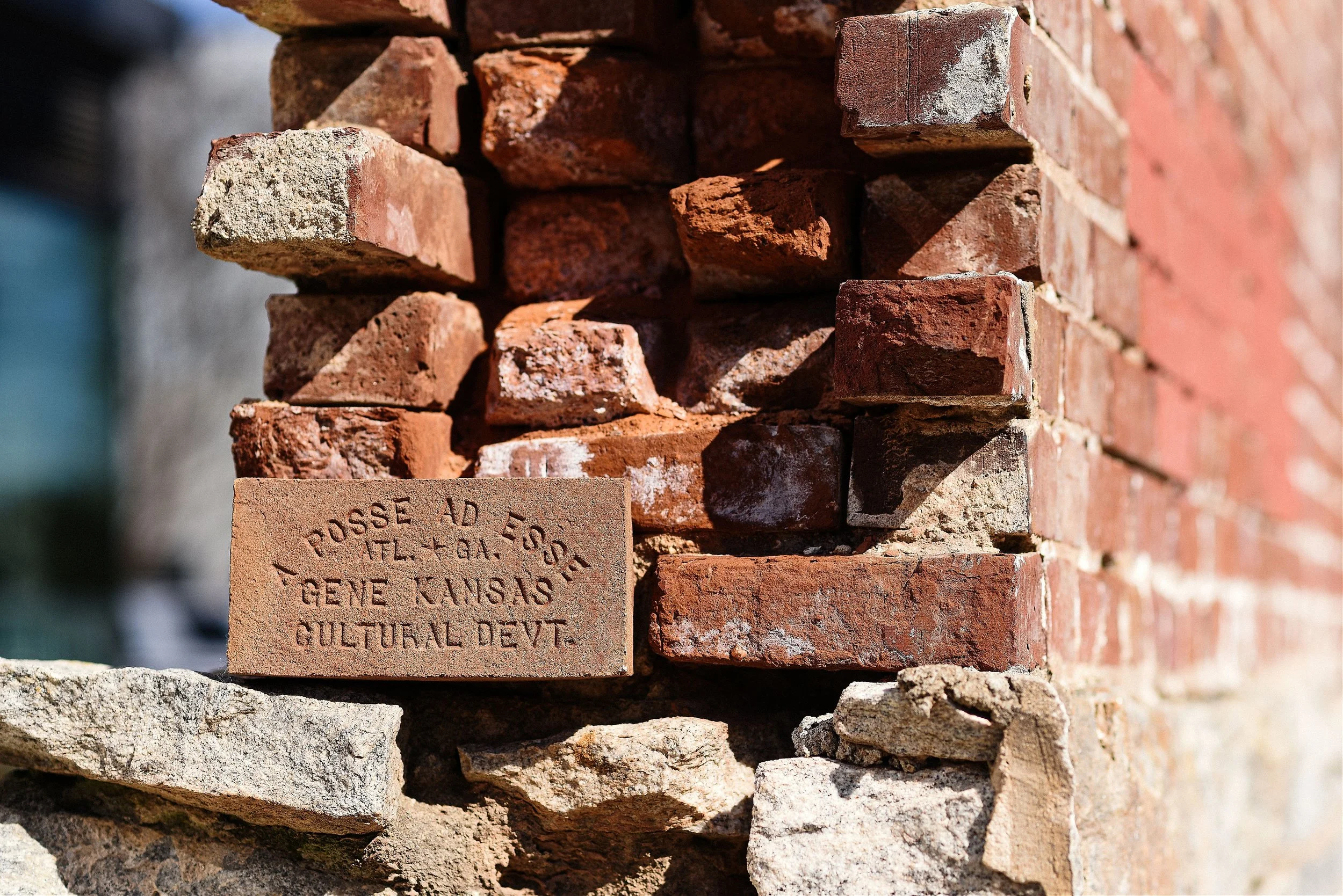 Close-up of a brick wall with an engraved brick that reads 'POSSE AD EOG' and mentions Geneva, Kansas, and cultural development.