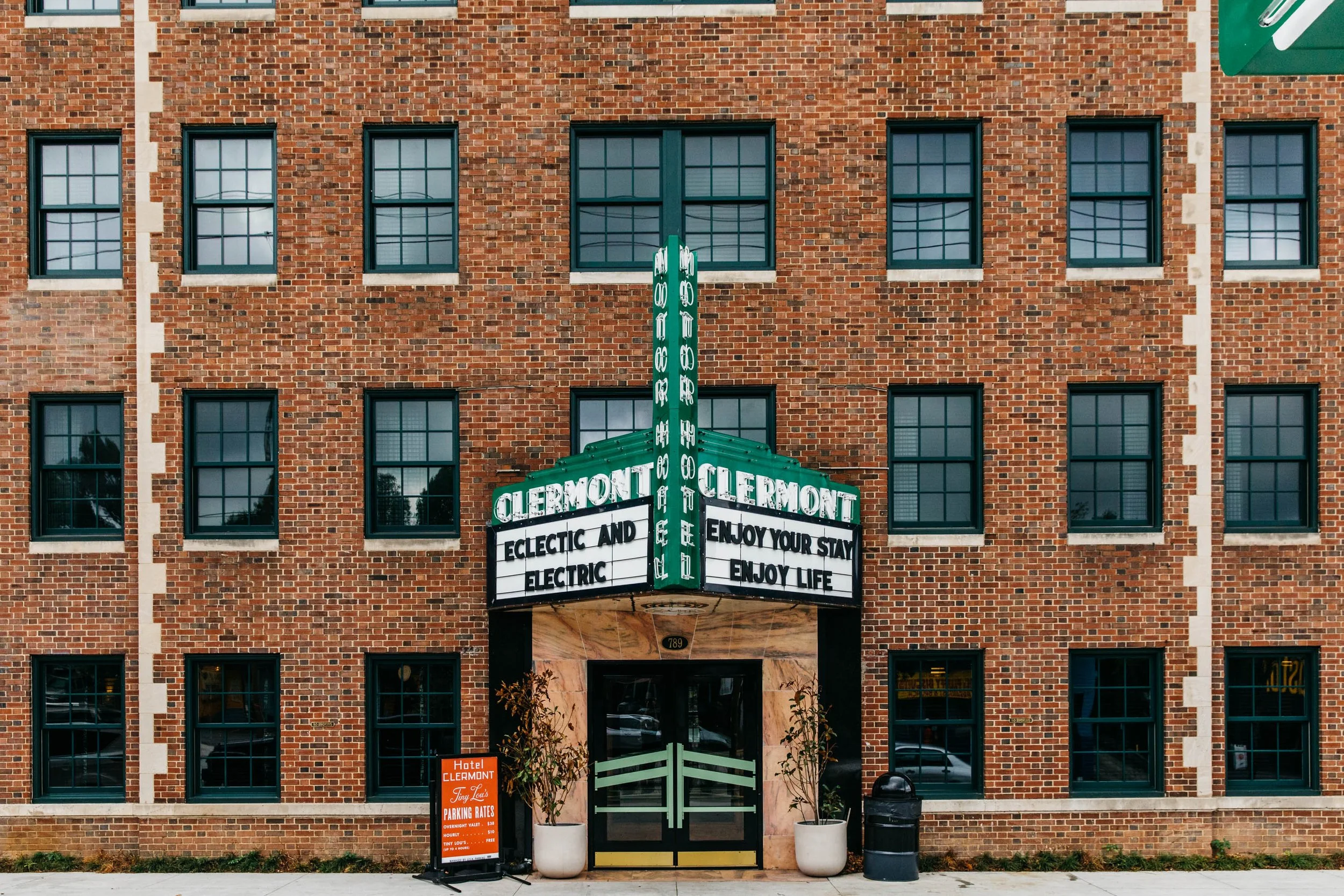 View of a brick building with multiple windows, a neon sign for Hotel Clermont, and an A-frame sign advertising parking rates.
