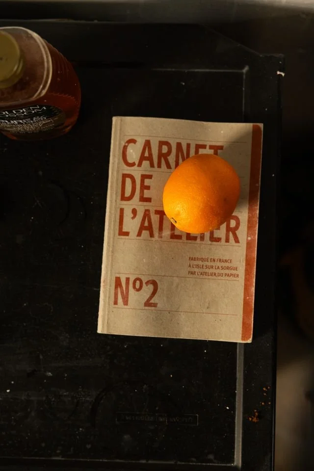 An orange resting on a French notebook titled 'Carnet de l'Atelier No2' on a black surface.