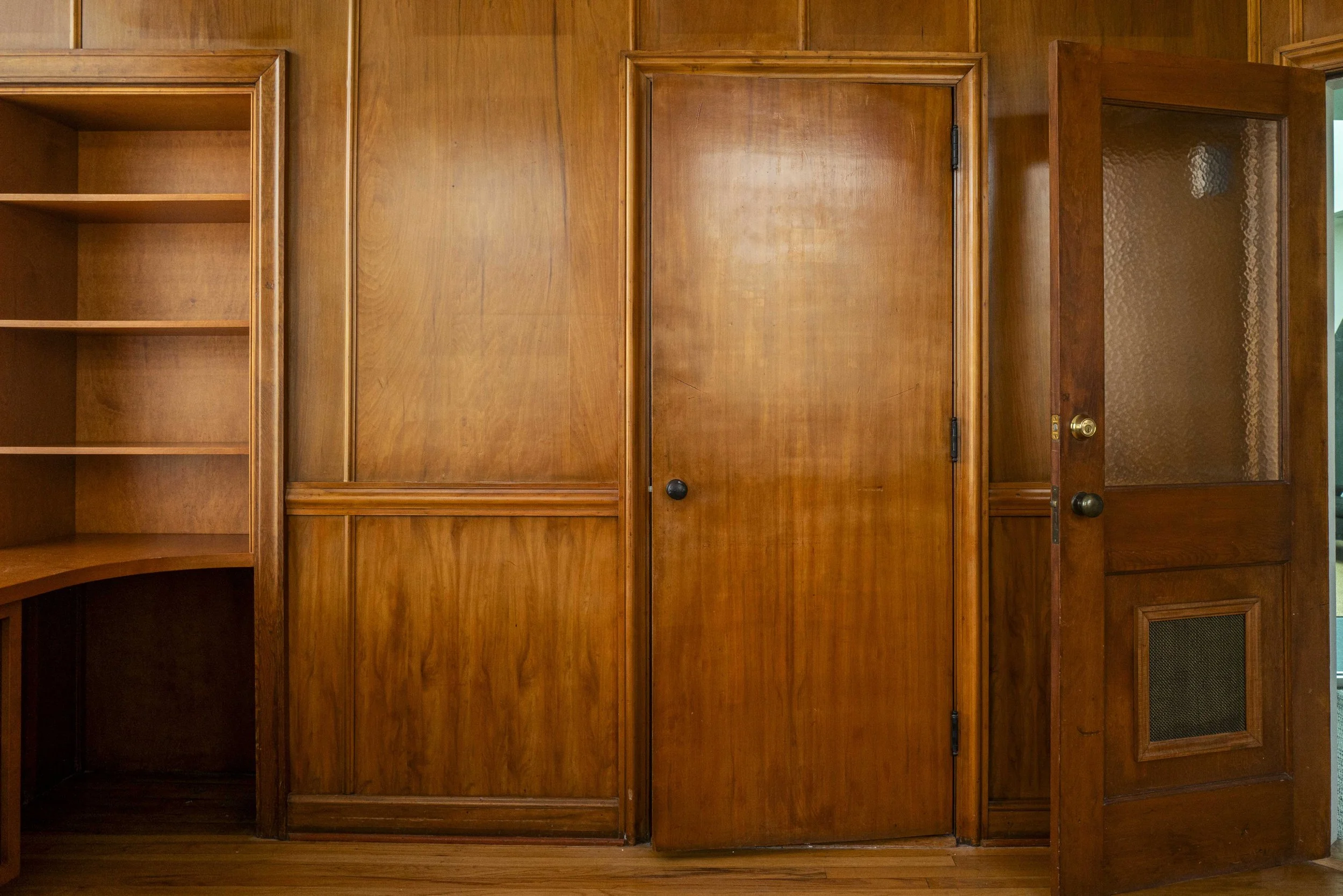 Wooden built-in cabinets with open and closed sections, some with glass doors, in a room with wooden flooring.