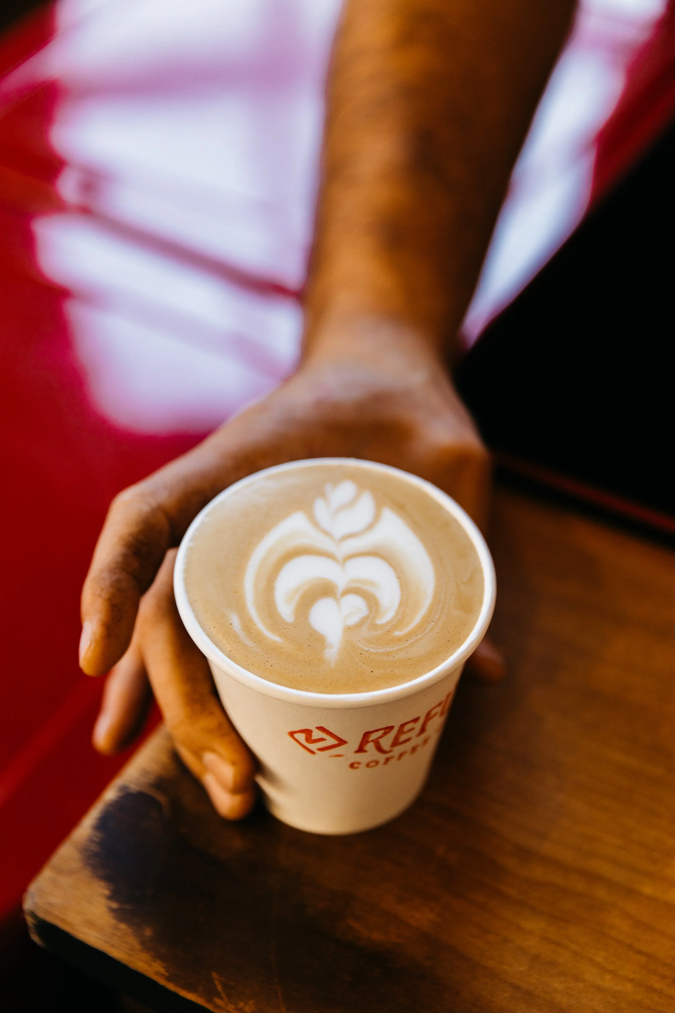Person holding a cup of coffee with latte art, sitting at a wooden table.