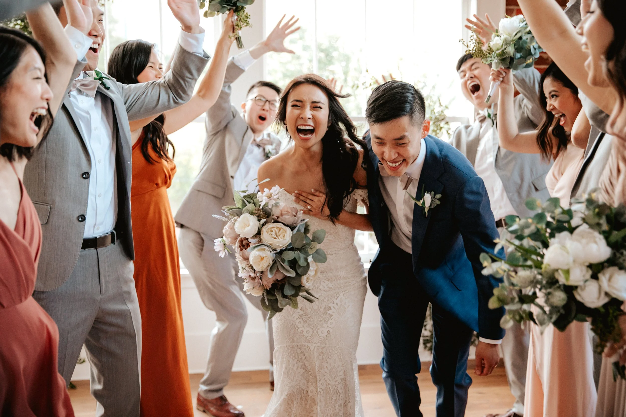 Bride and groom at Constellations in Sweet Auburn, are surrounded by friends and family celebrating during a wedding reception, all smiling, cheering, and raising their hands.