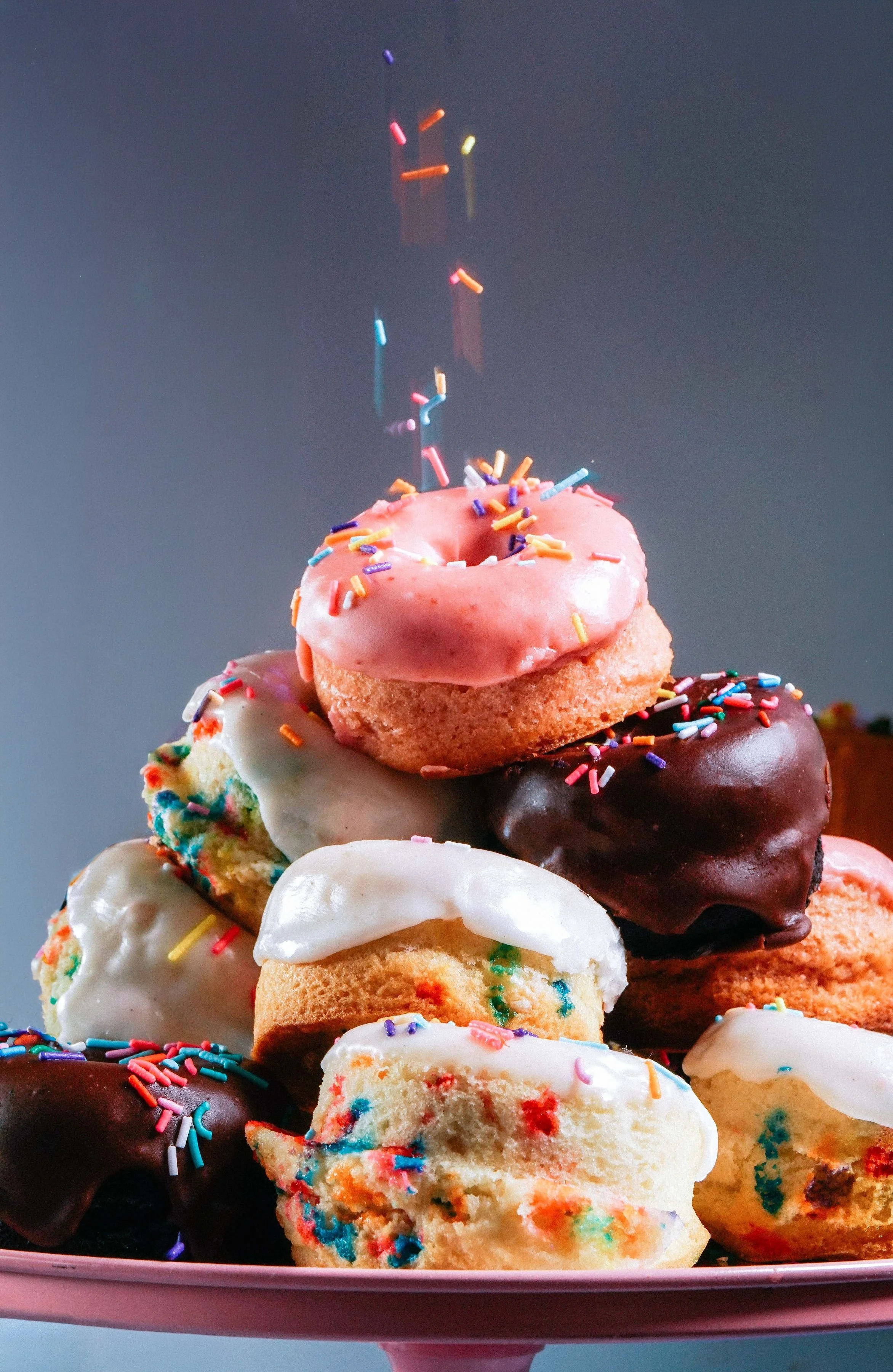 A plate of assorted colorful donuts with sprinkles, glazed and chocolate toppings.