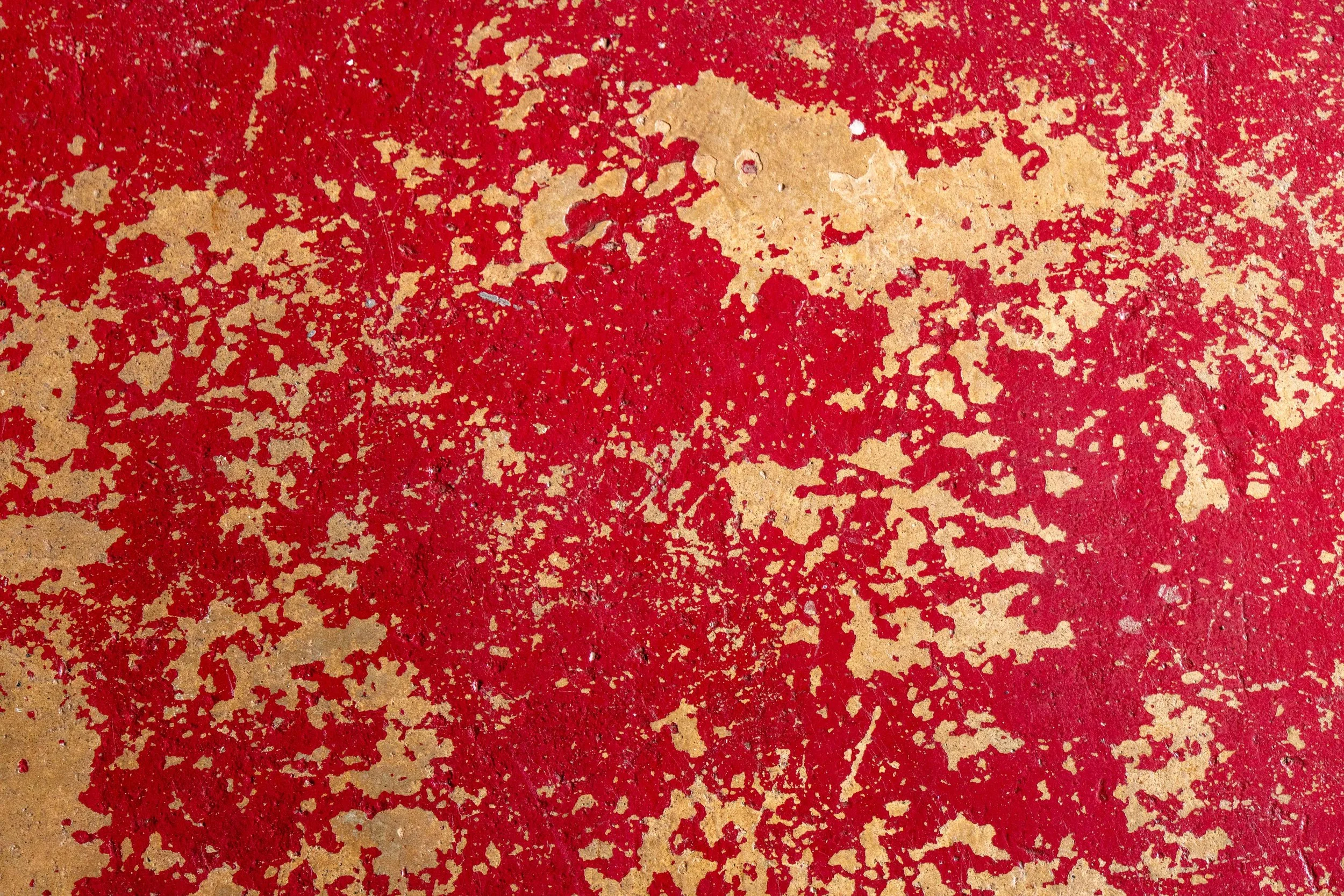 Close-up of a rusty surface with peeling red and beige paint.