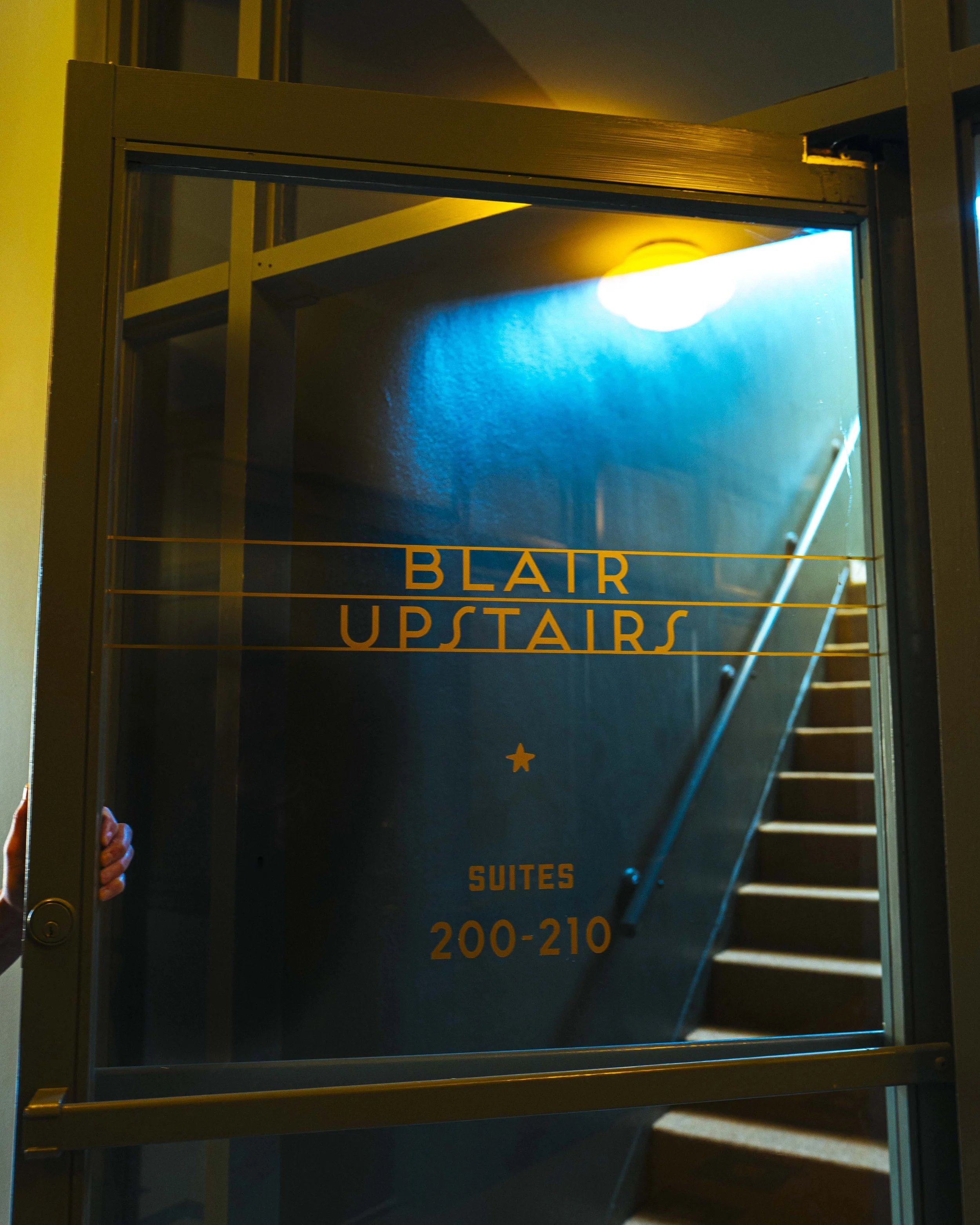 The Blair Building stairwell glass door with gold lettering indicating floors 200-210, with stairs visible inside and a small star at the bottom