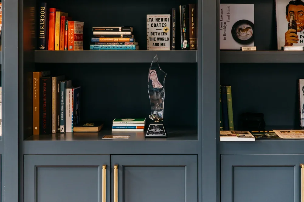 Blue bookshelves filled with various books, a glass award, and some magazines or pamphlets.