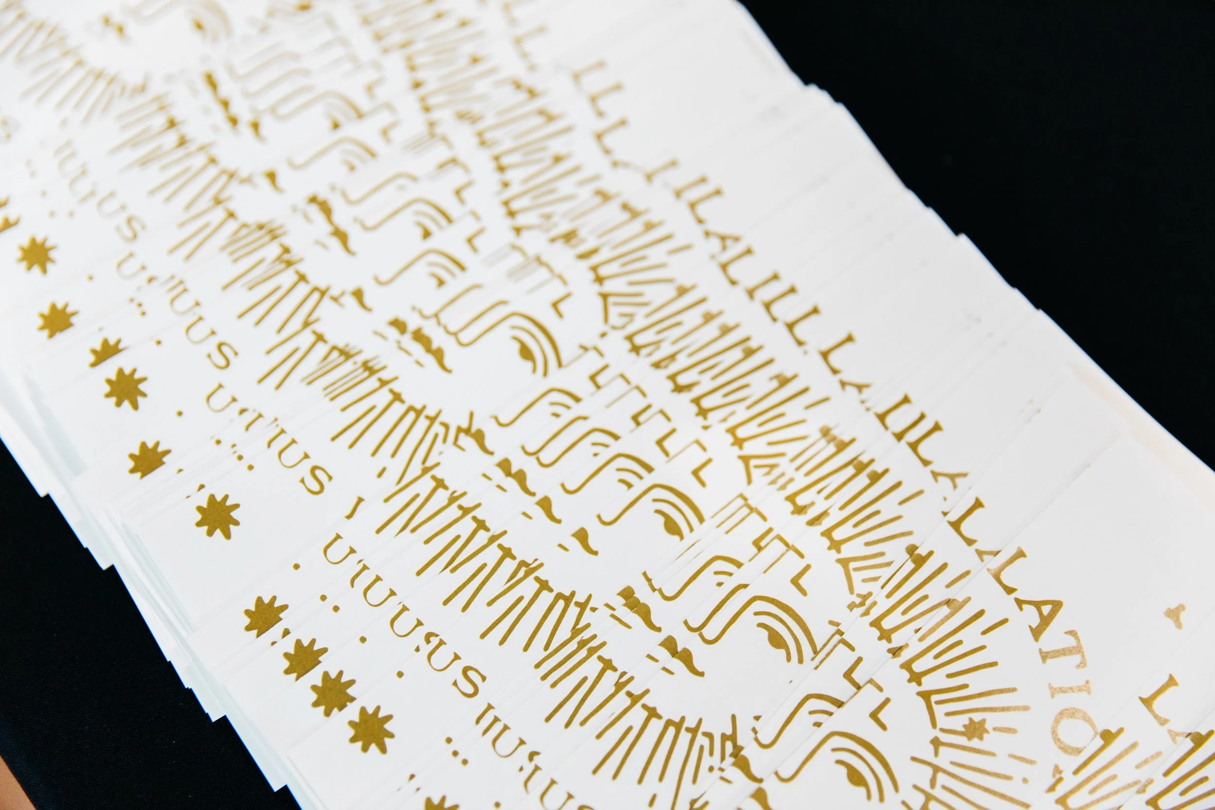 Close-up of gold foil stickers with decorative text and star symbols on white backing, partially overlapping.