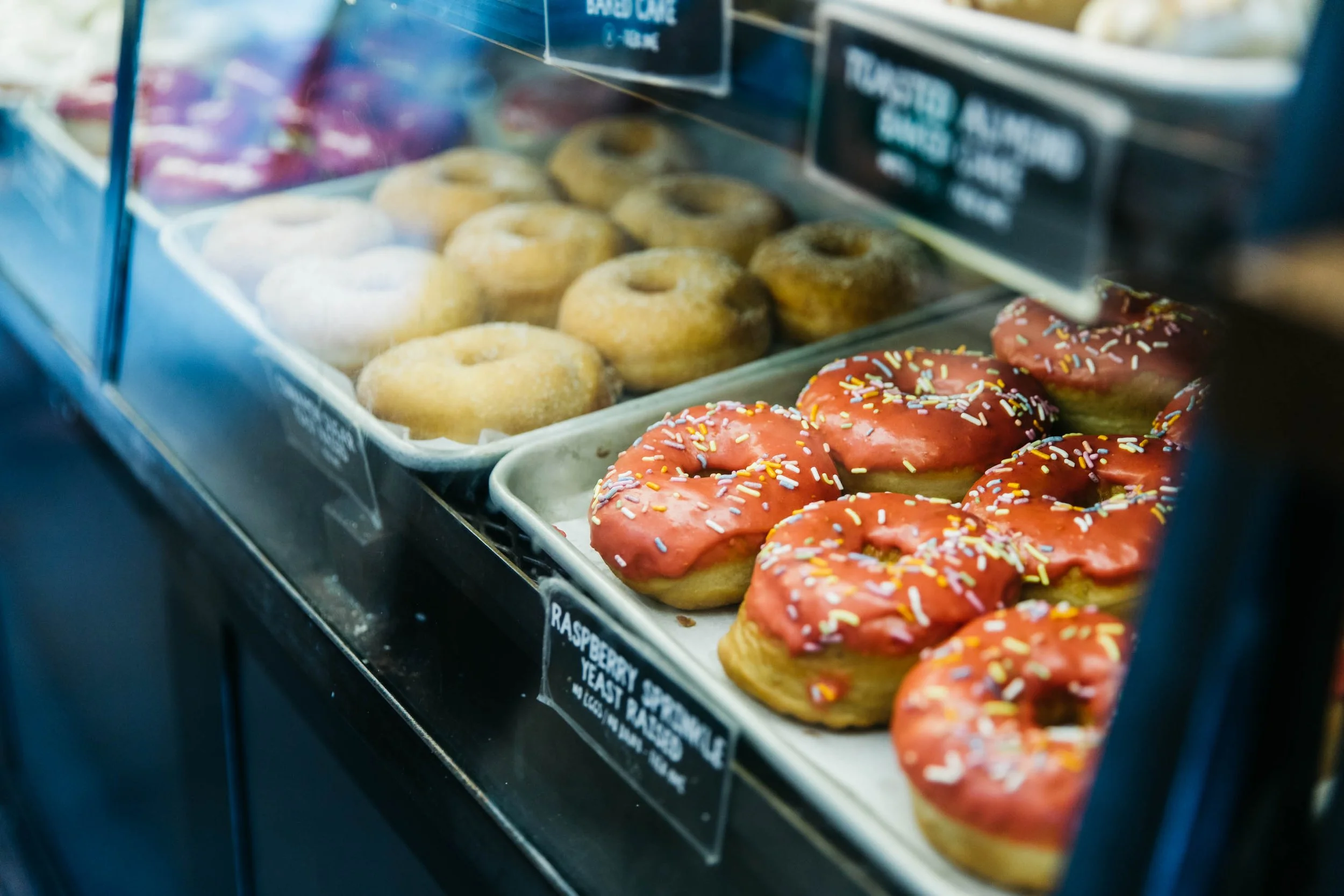 Display case with donuts, including classic glazed and pink frosted donuts with sprinkles.